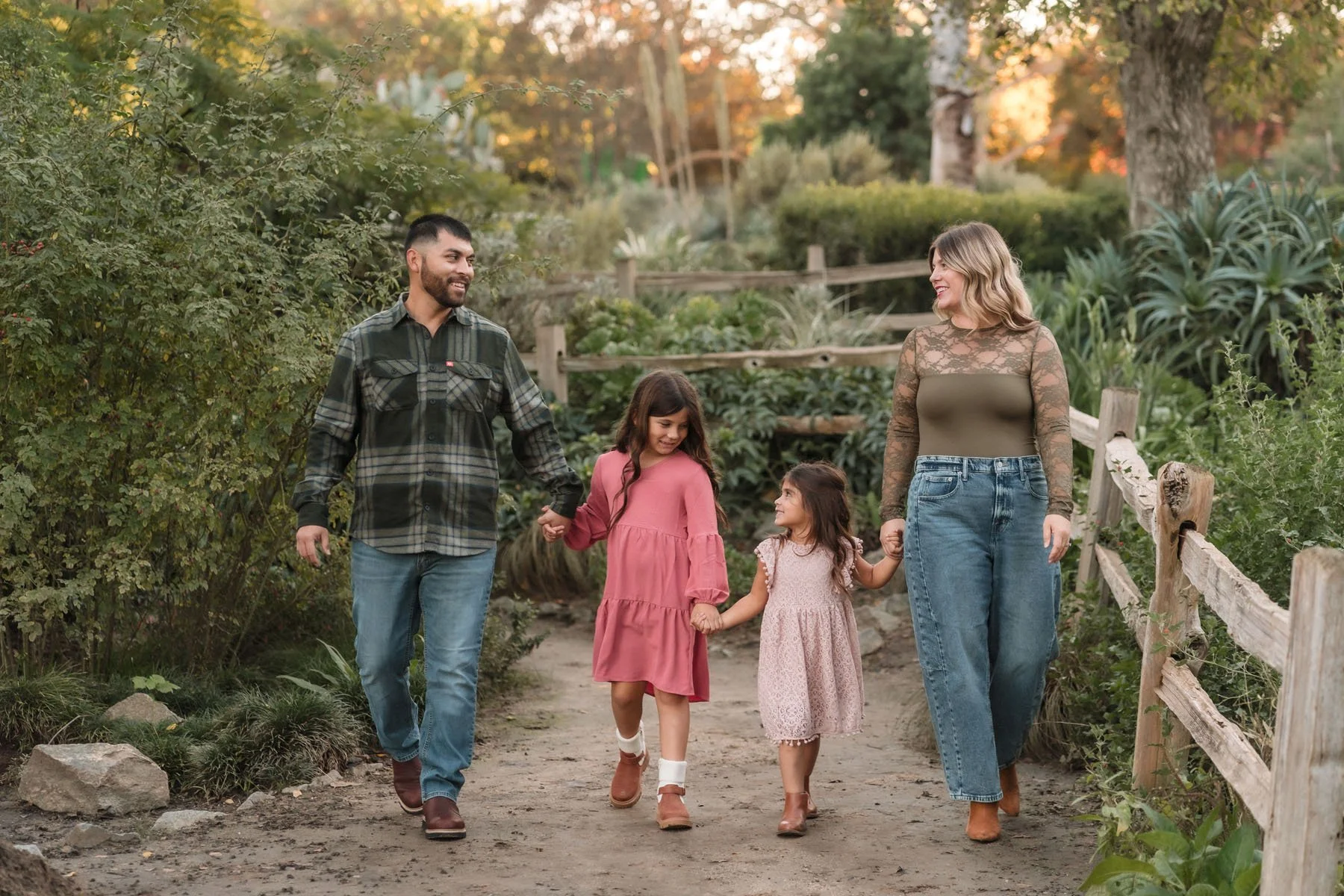 A family of four walking together on a trail in a lush, green park during their family photos at the WPA Rock Garden with Katherine Nicole Photography.