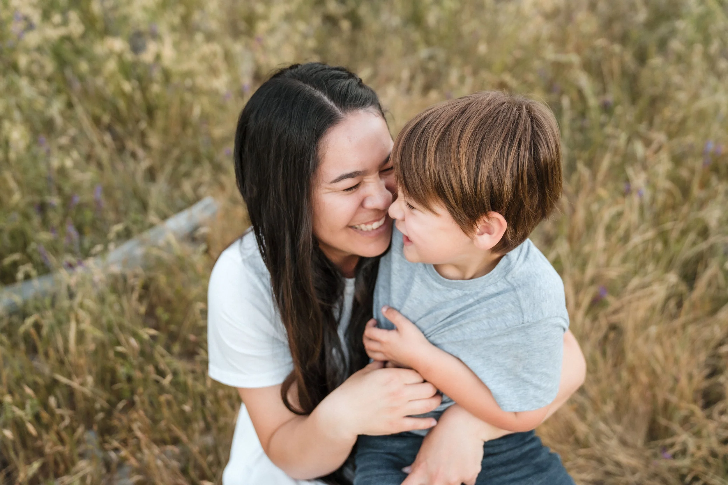 A woman and a young boy sharing a joyful hug in a field of tall grass and wildflowers while taking family photos with Sacramento family photographer Katherine Nicole Photography. 