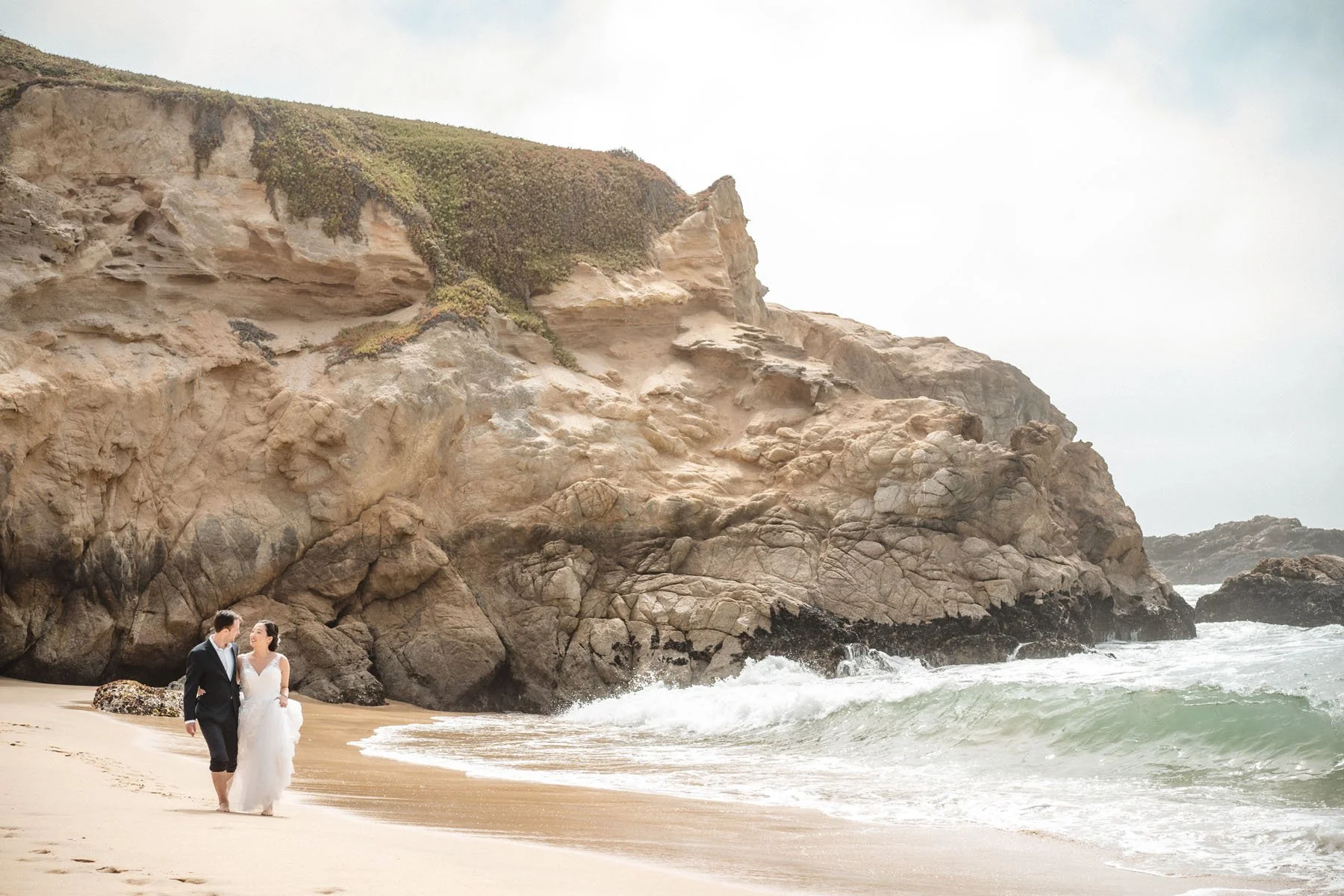 Bride and groom walk on the beach in half moon bay on the day of their elopement