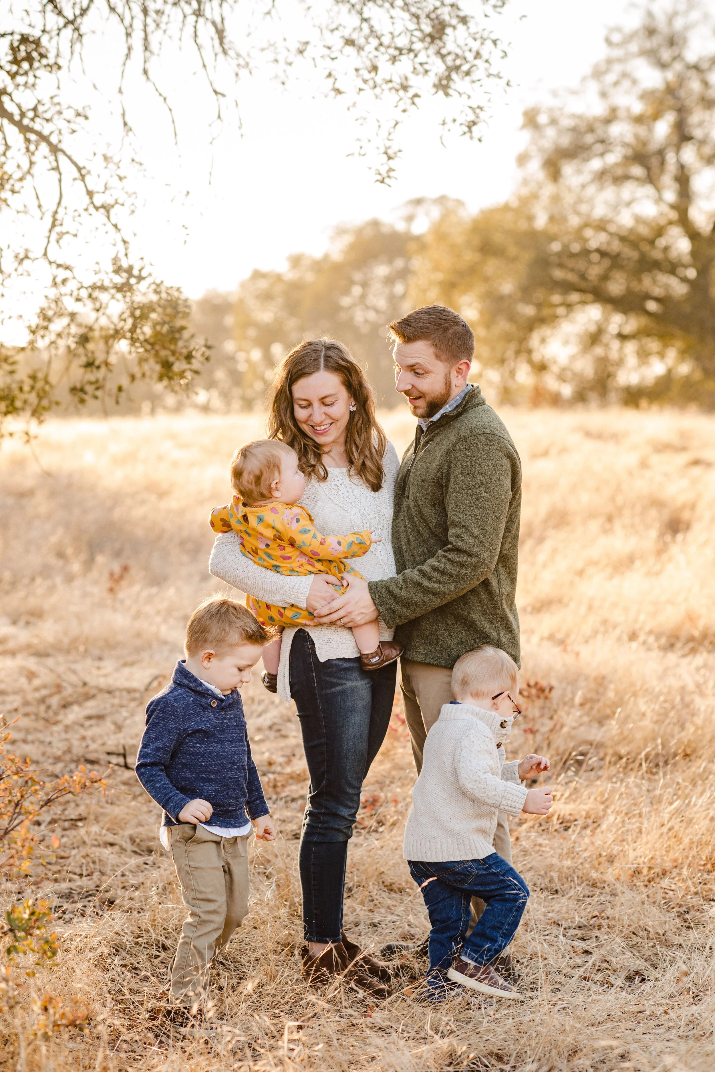 A family enjoying a walk outdoors in a field during autumn, with trees in the background and warm sunlight, while taking family photos with Sacramento family photographer Katherine Nicole Photography. 