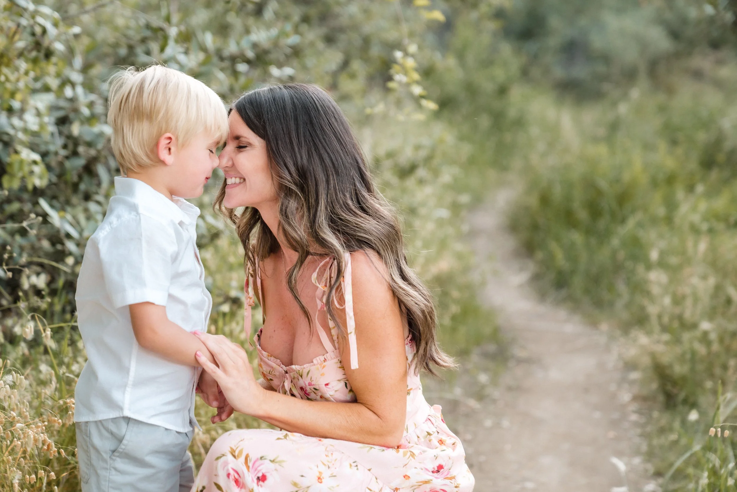 A woman and young boy sharing a tender moment outdoors, touching foreheads with eyes closed, surrounded by greenery, during family photos with Sacramento family photographer Katherine Nicole Photography. 