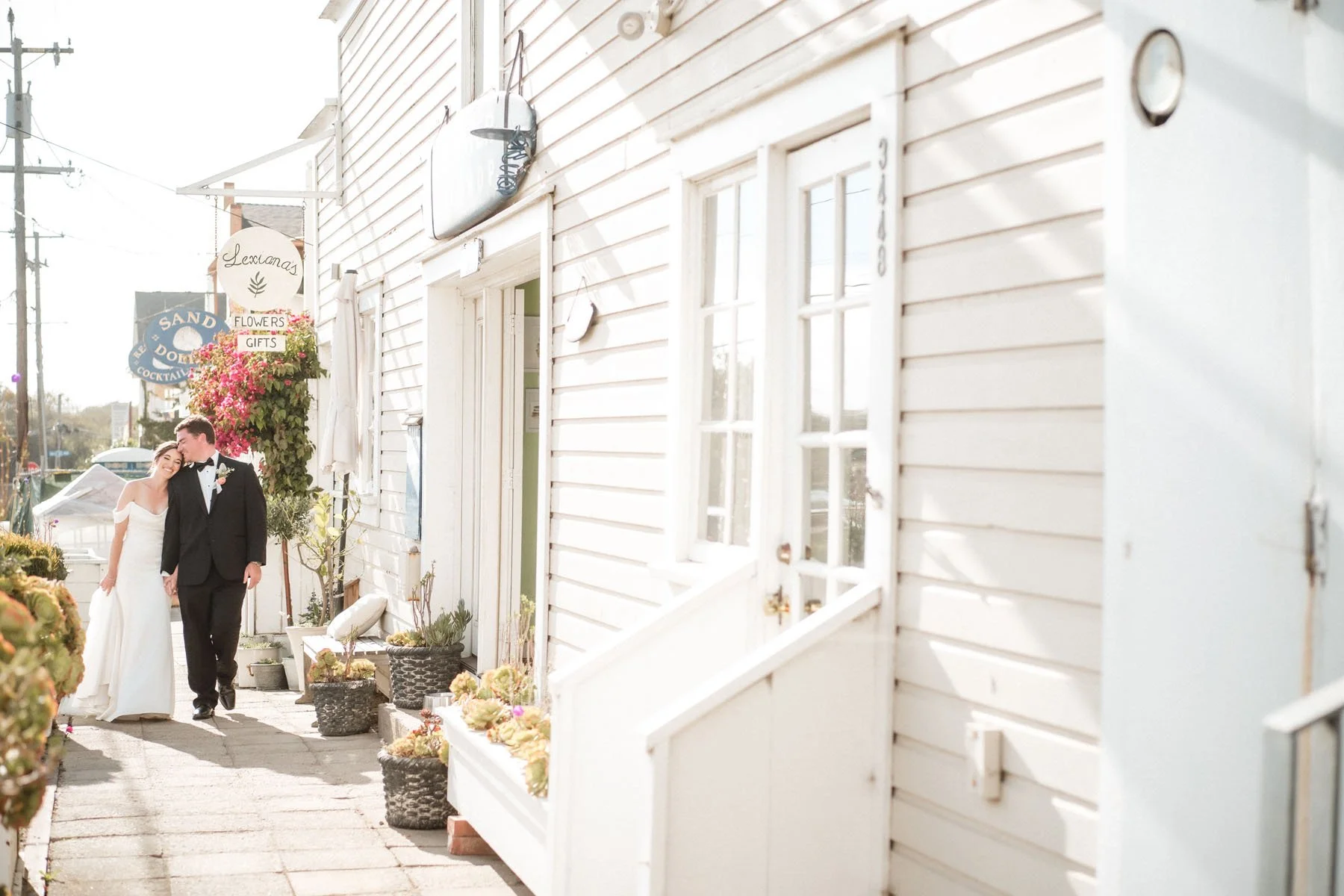 A bride and groom walking arm in arm down the street near Stinson Beach, with flowers and plants along the sidewalk. Photography by Sacramento wedding photographer Katherine Nicole Photography.