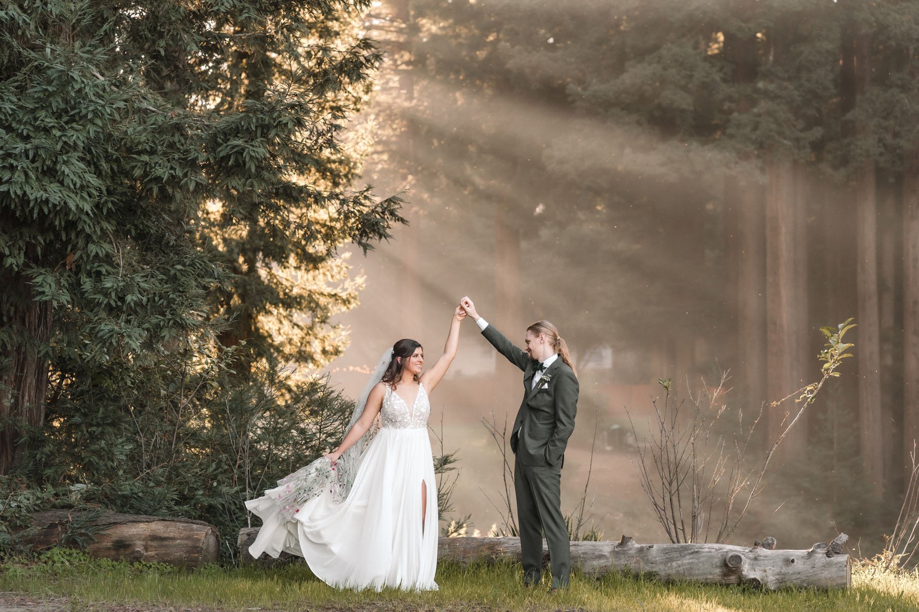 A bride and groom holding hands and dancing outdoors at their Mountain Terrace wedding. Sunlight filters through the trees in the background. Photography by Sacramento wedding photographer Katherine Nicole Photography.