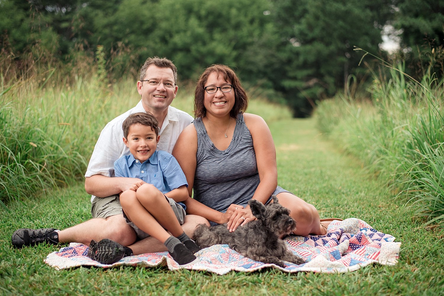 Family of 3 with dog sitting in field