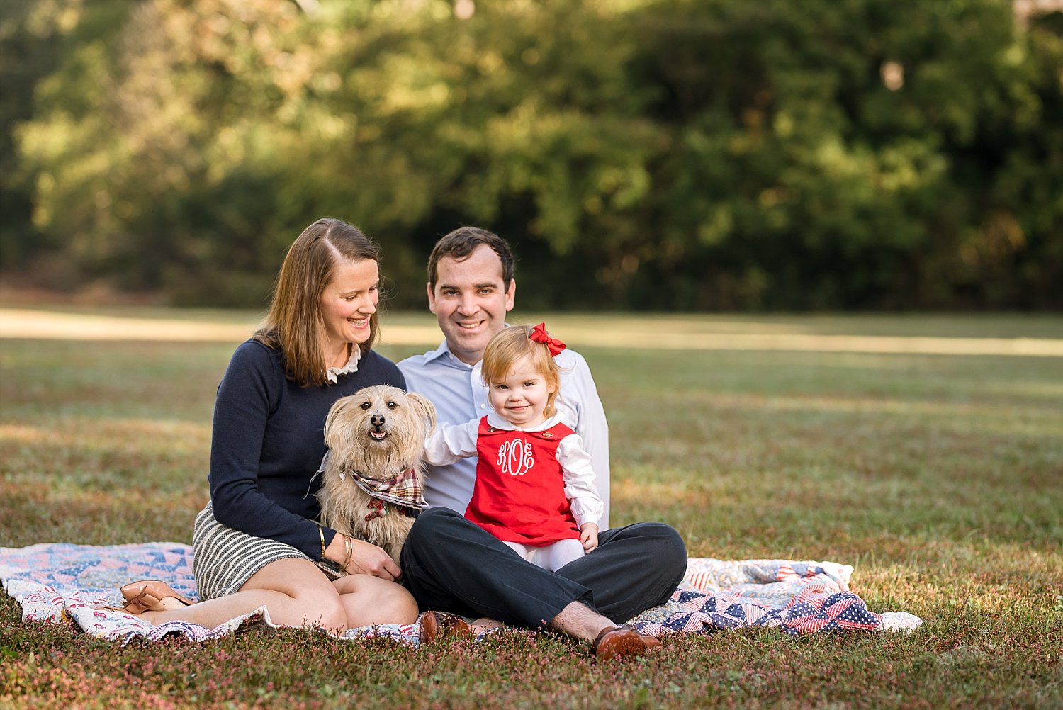 Family of 3 with dog on blanket in park