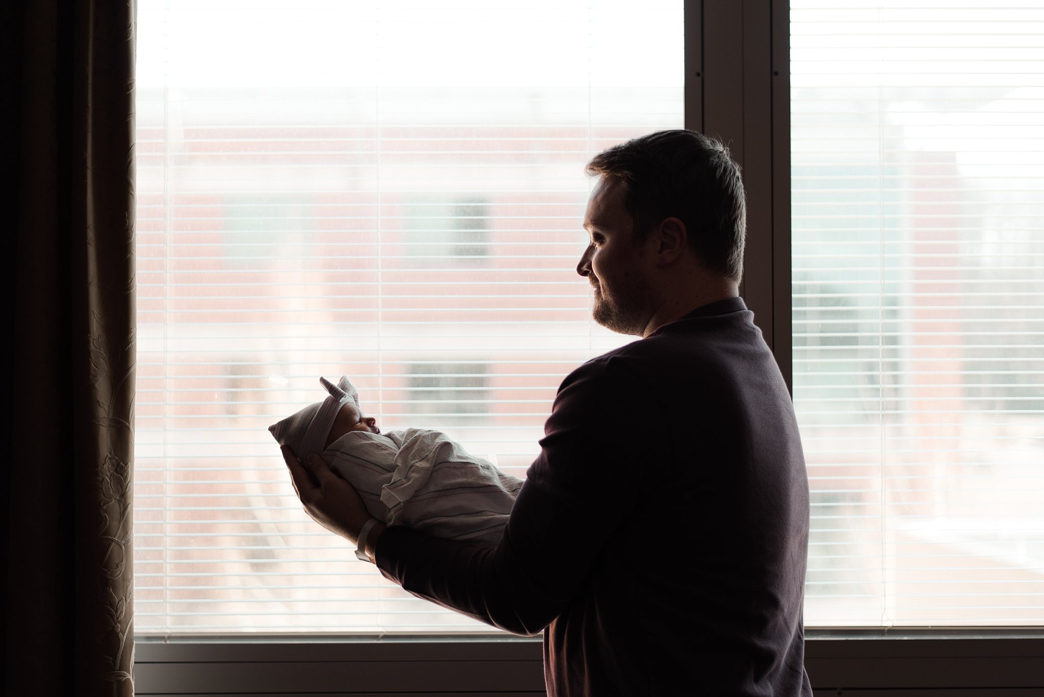 silhouette of dad with baby girl in front of window at hospital