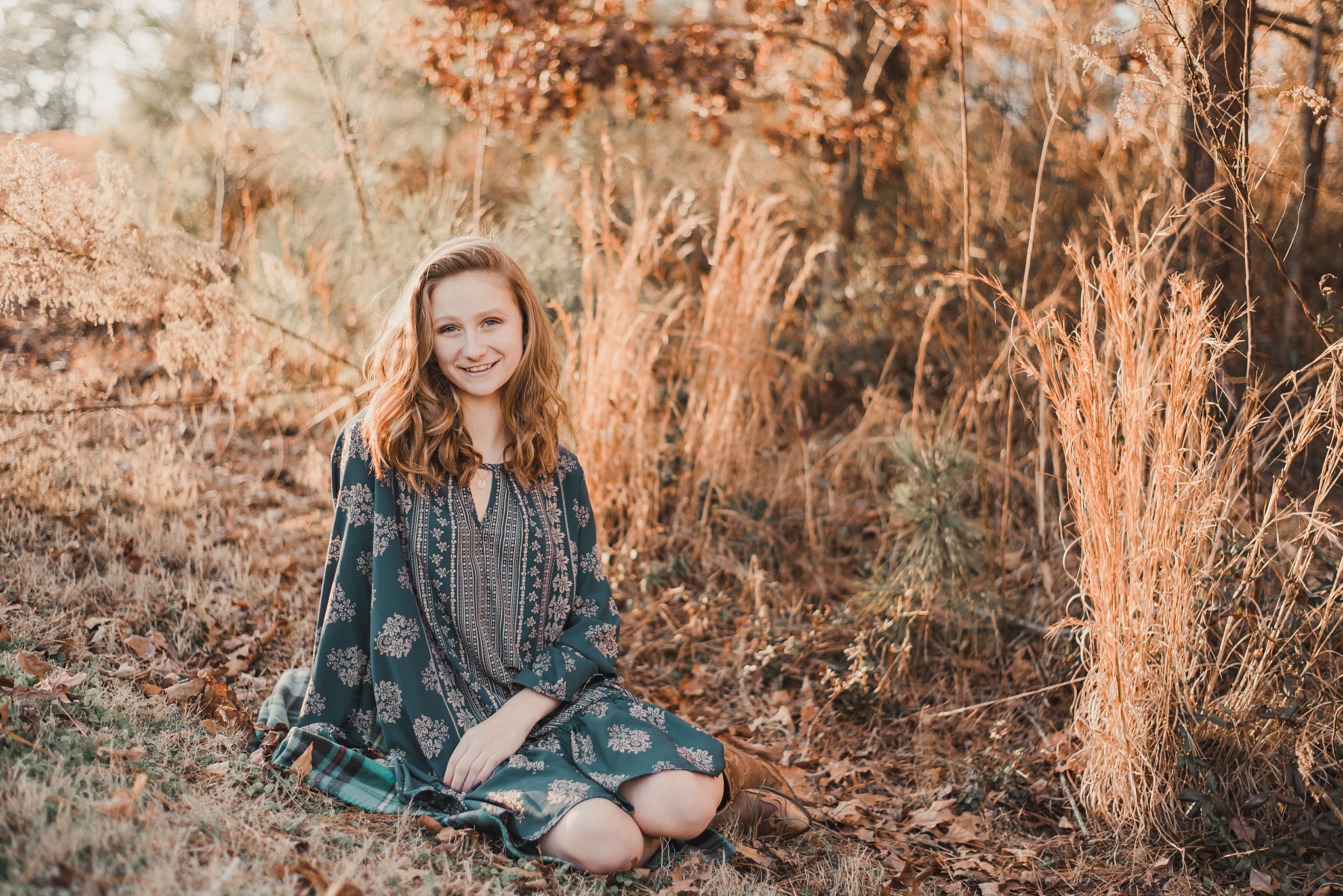 senior girl sitting in tall grass at golden hour