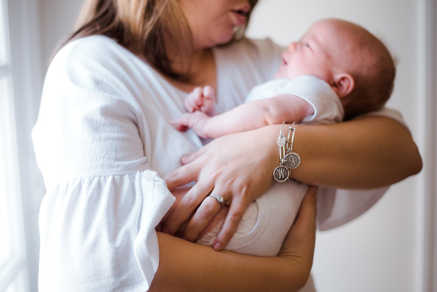 close up of mothers intial bracelets holding newborn baby