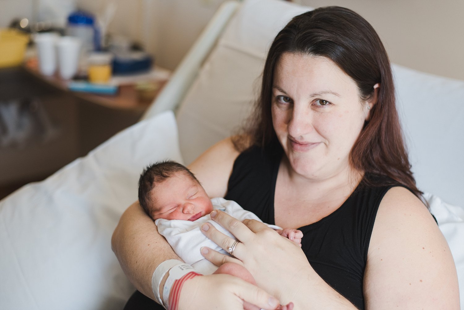 mother holding newborn baby son in hospital bed