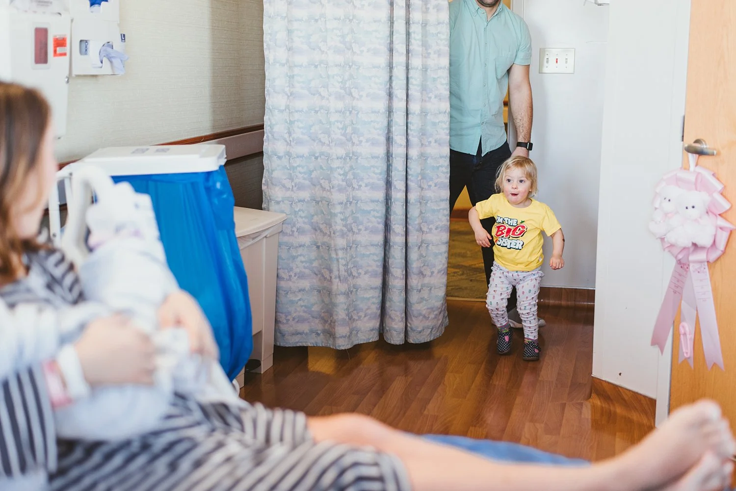 toddler girl in walking in to hospital room to meet sister's for first time 
