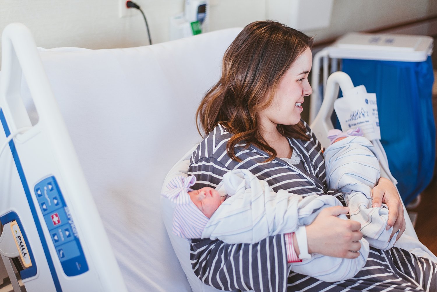 mom holding twin newborn girls in hospital bed