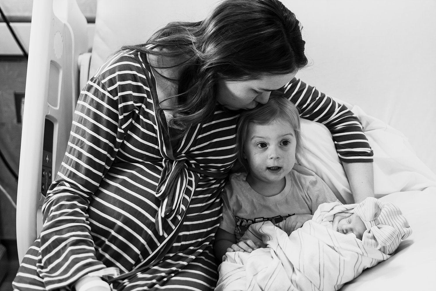 Mother kissing toddler holding newborn baby sister at Northside Atlanta Hospital