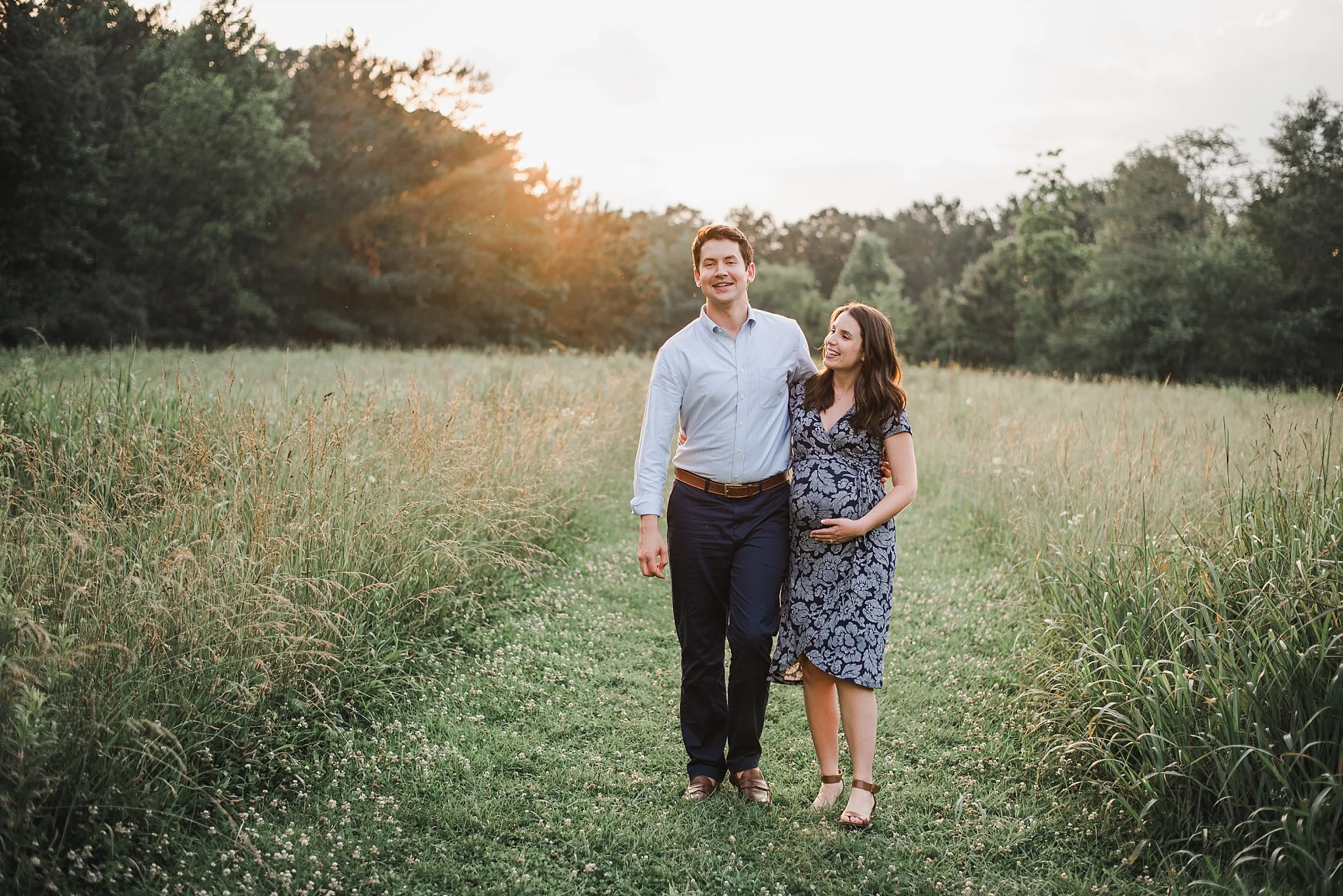 Expecting couple walking in field of tall grass at Green Meadows Preserve