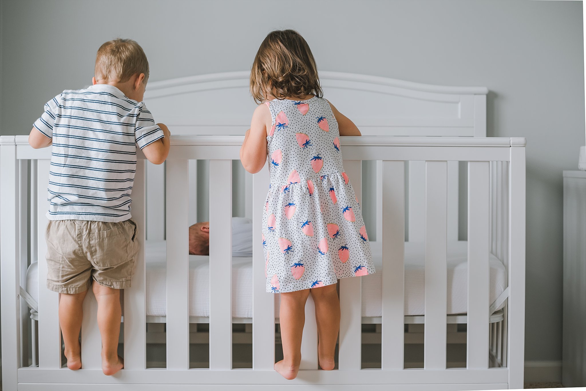 twins standing on crib looking at newborn baby boy