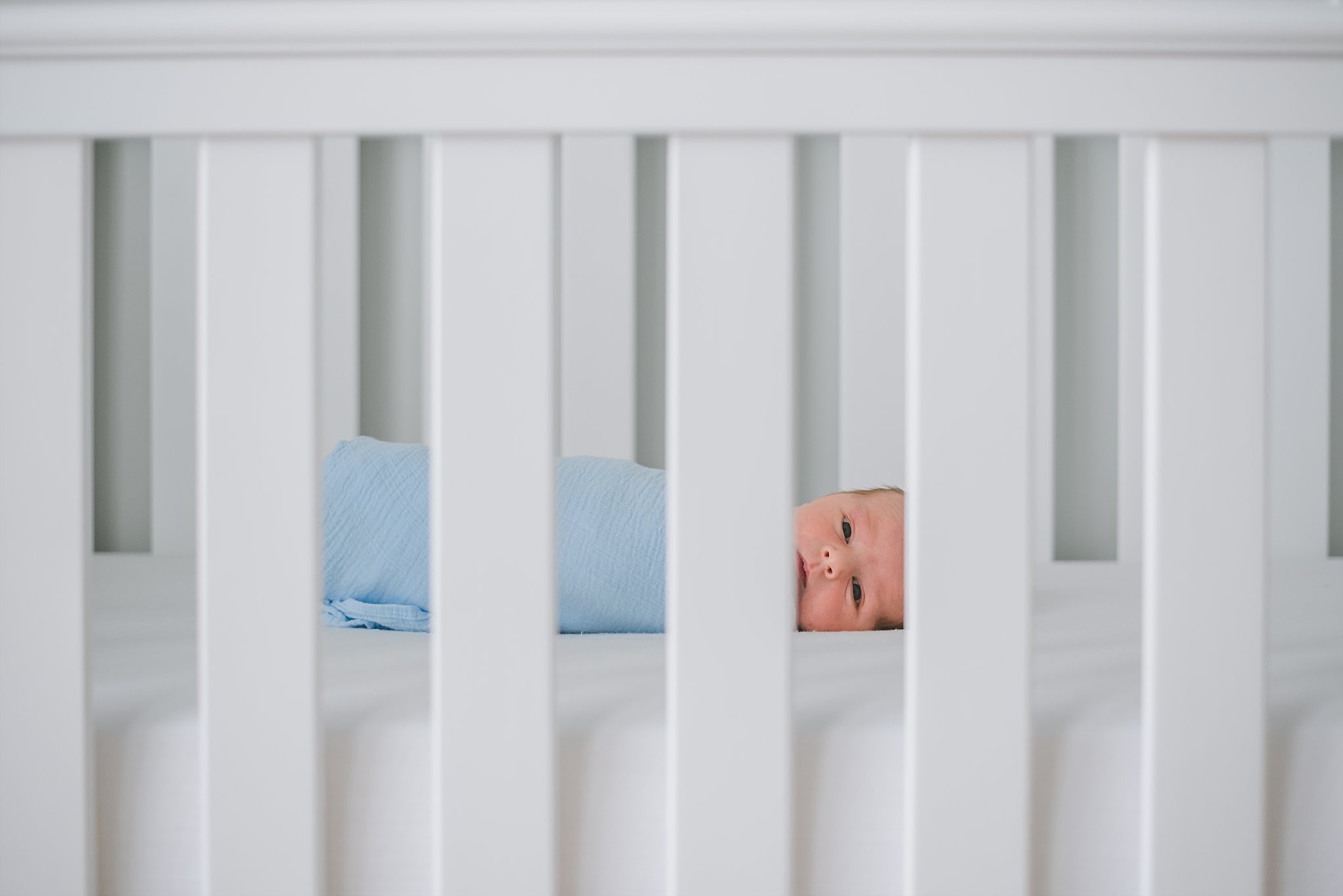 newborn baby boy swaddled looking through crib slats