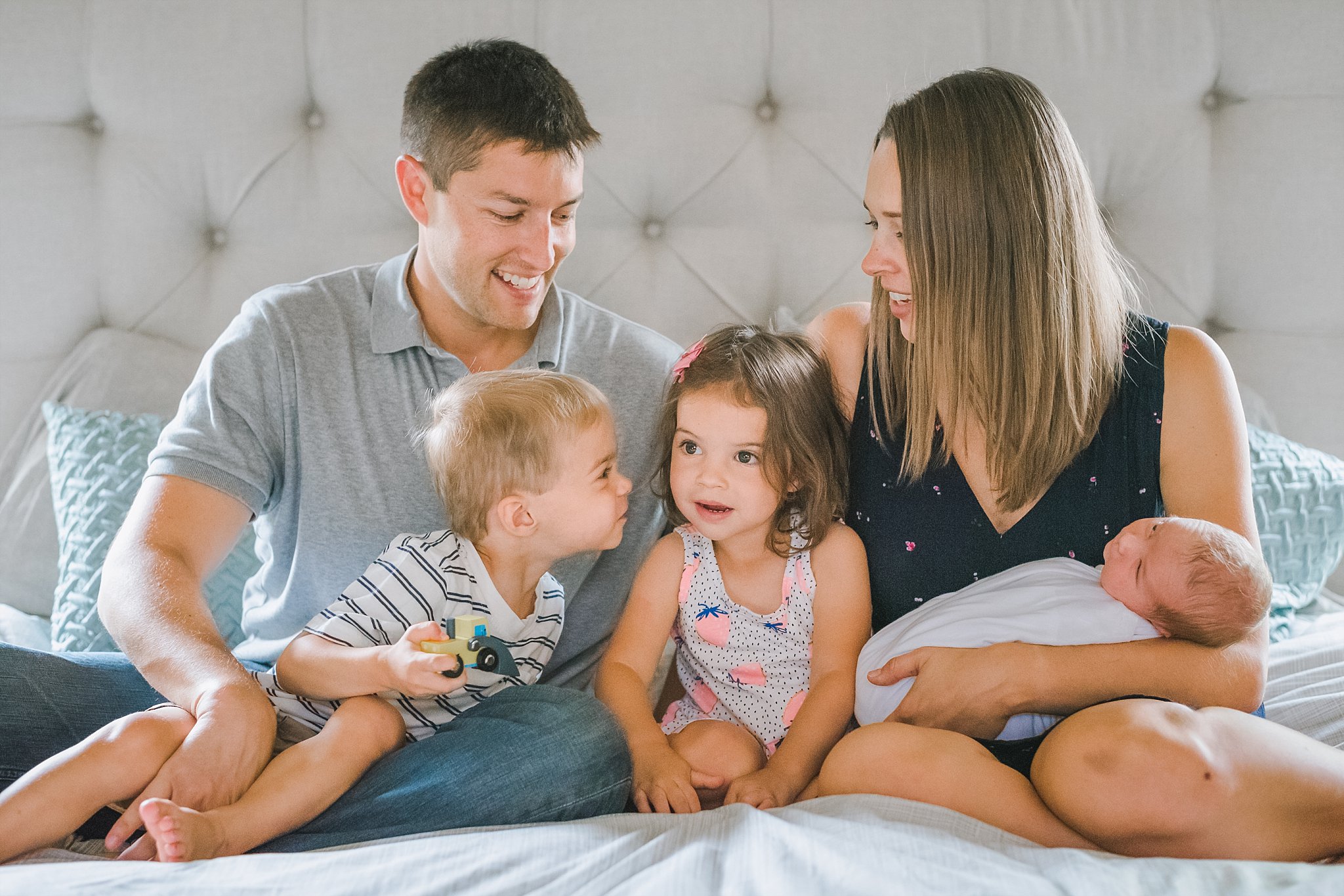 family of 5 sitting on bed with newborn