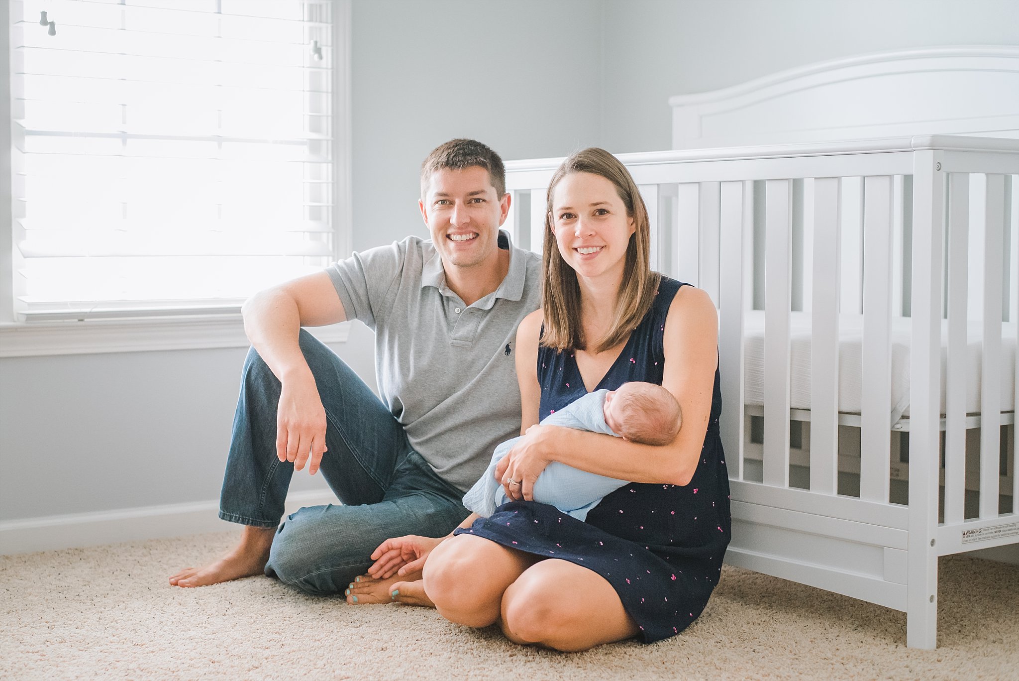 Mother and father with newborn in nursery sitting in front of crib