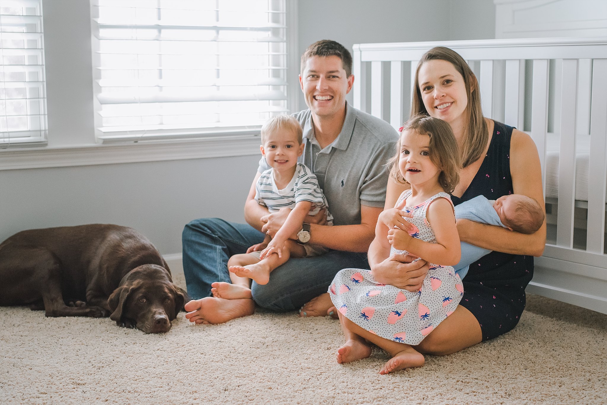 Family of 5 with dog in front of crib 