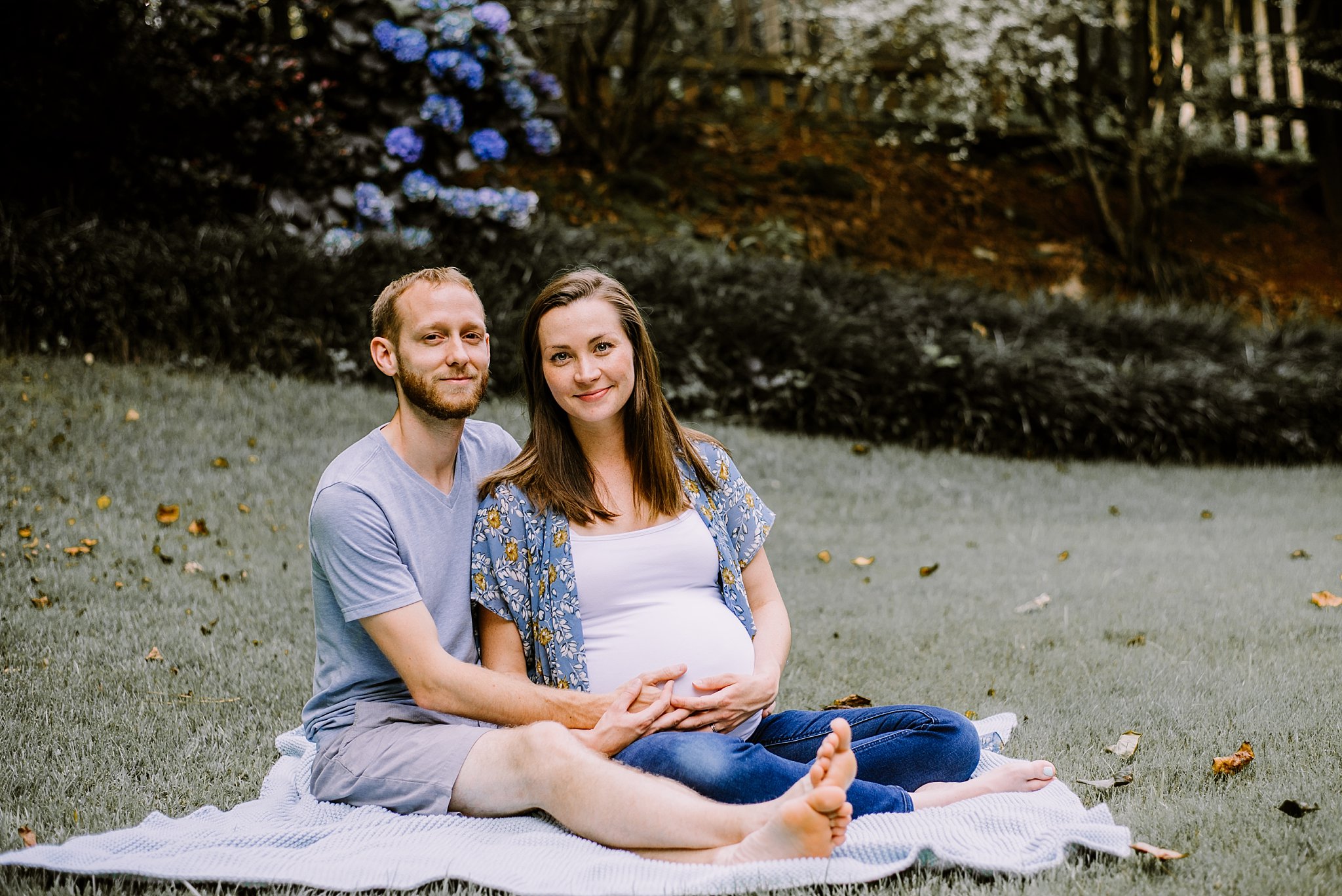 couple sitting in grass holding pregnant mother's belly