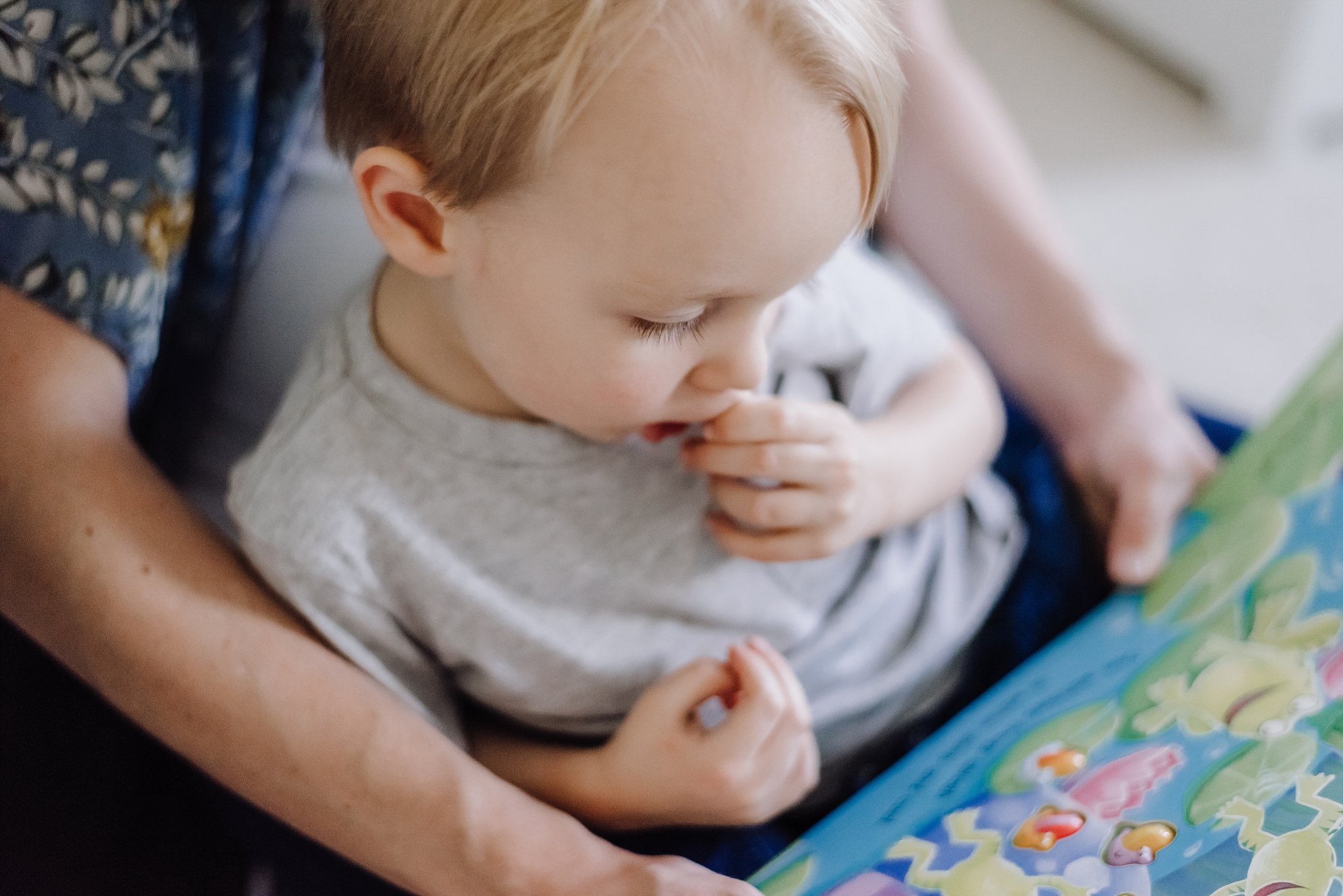 close up of toddler boy looking at book with mother