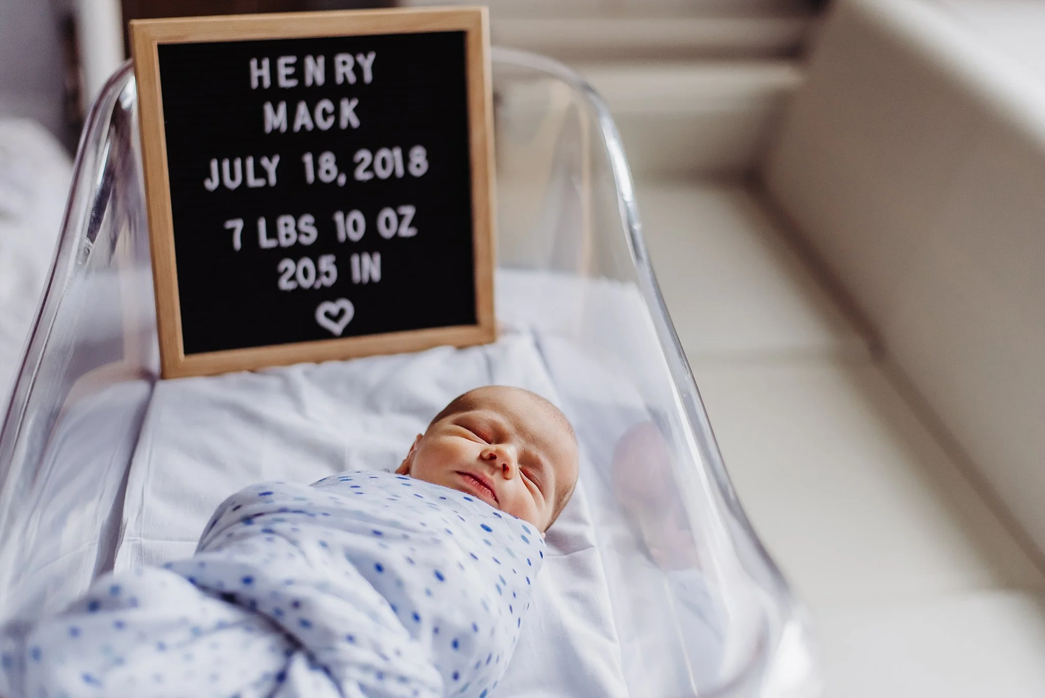 newborn baby boy in hospital bassinet with birthdate, name and weight on letterboard