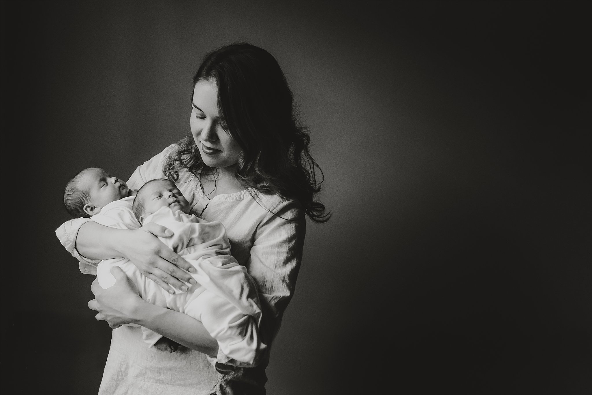 black and white portrait of mother looking at newborn twins