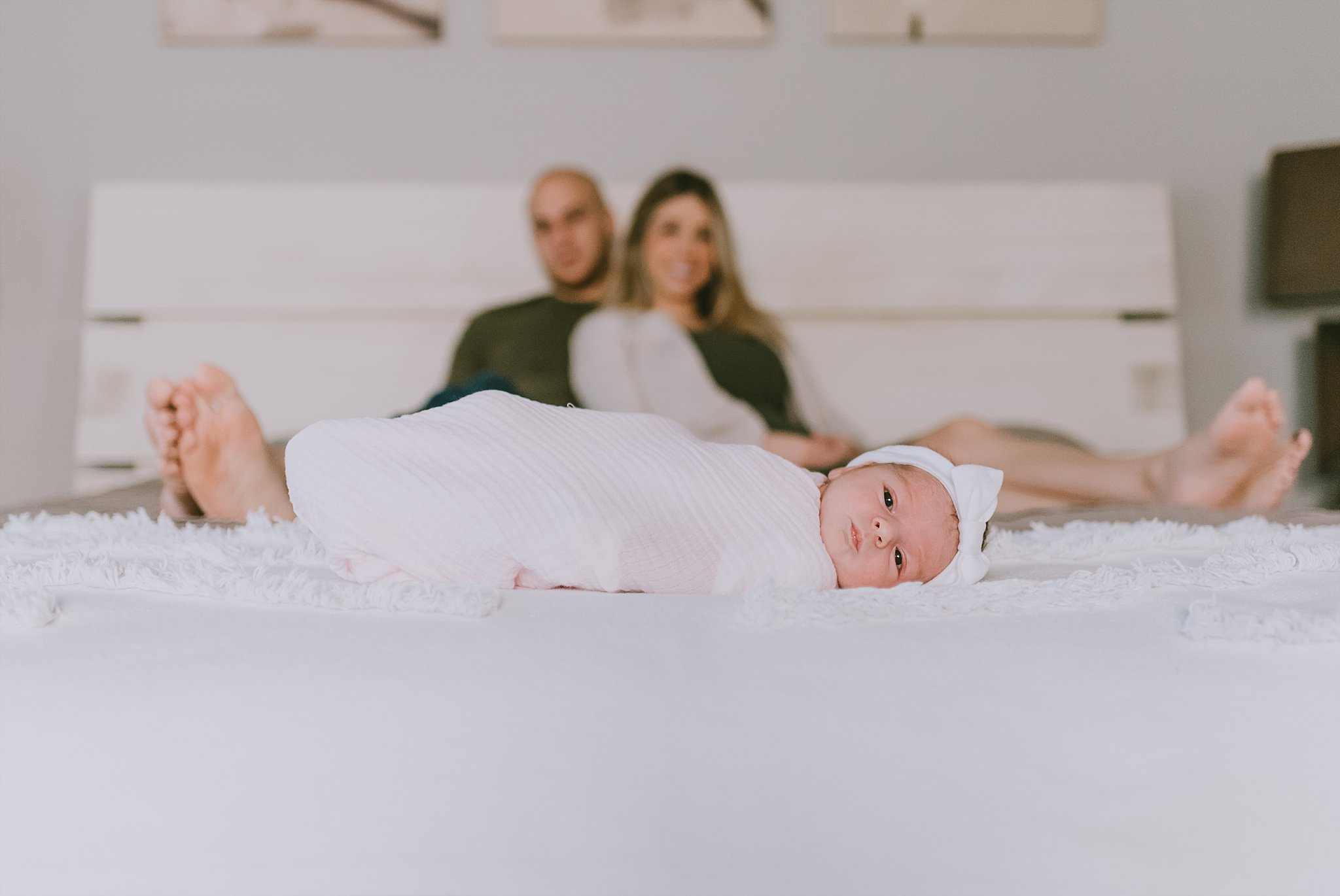 baby girl swaddled on bed parents in background
