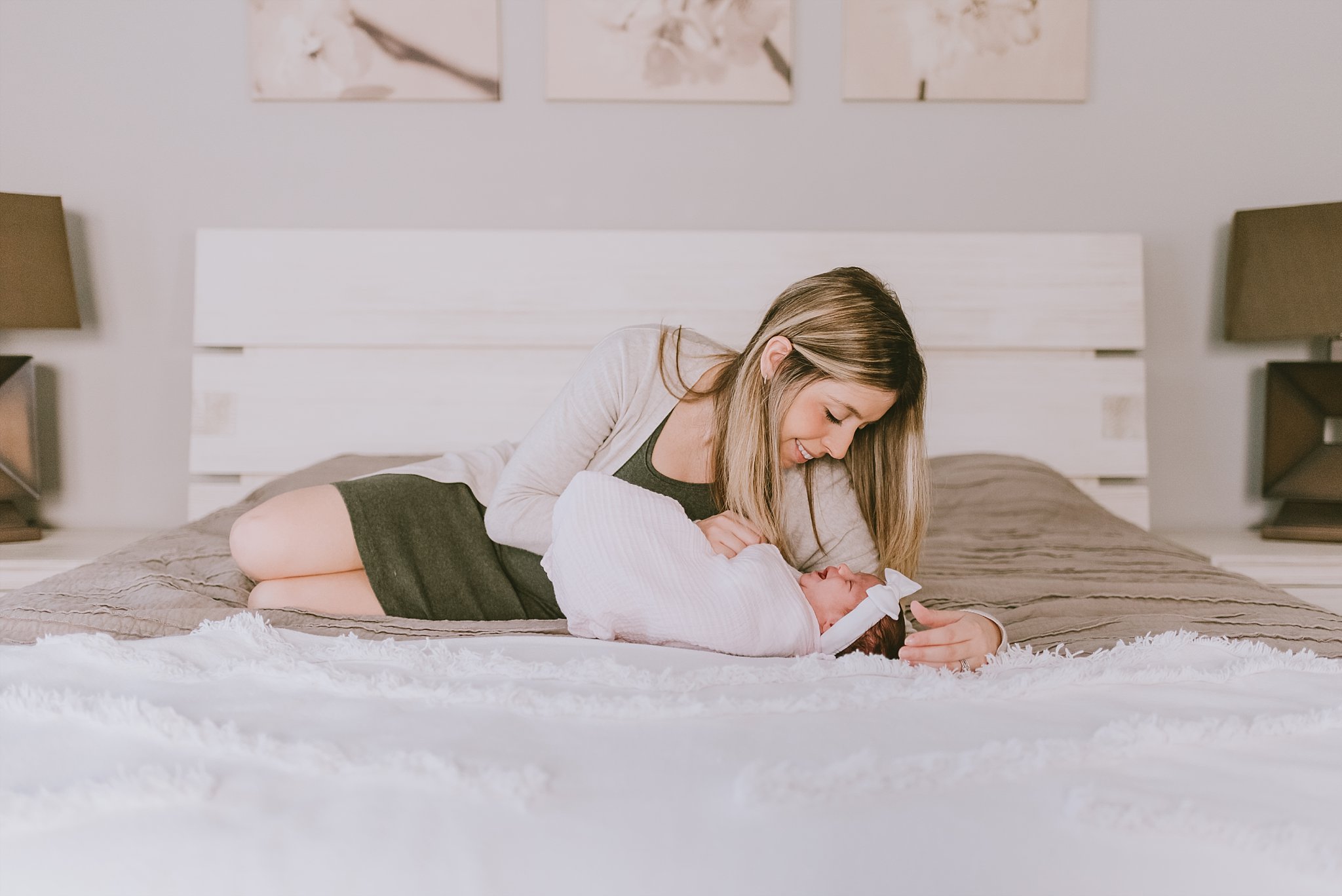 mom laying on bed looking at newborn baby girl swaddled
