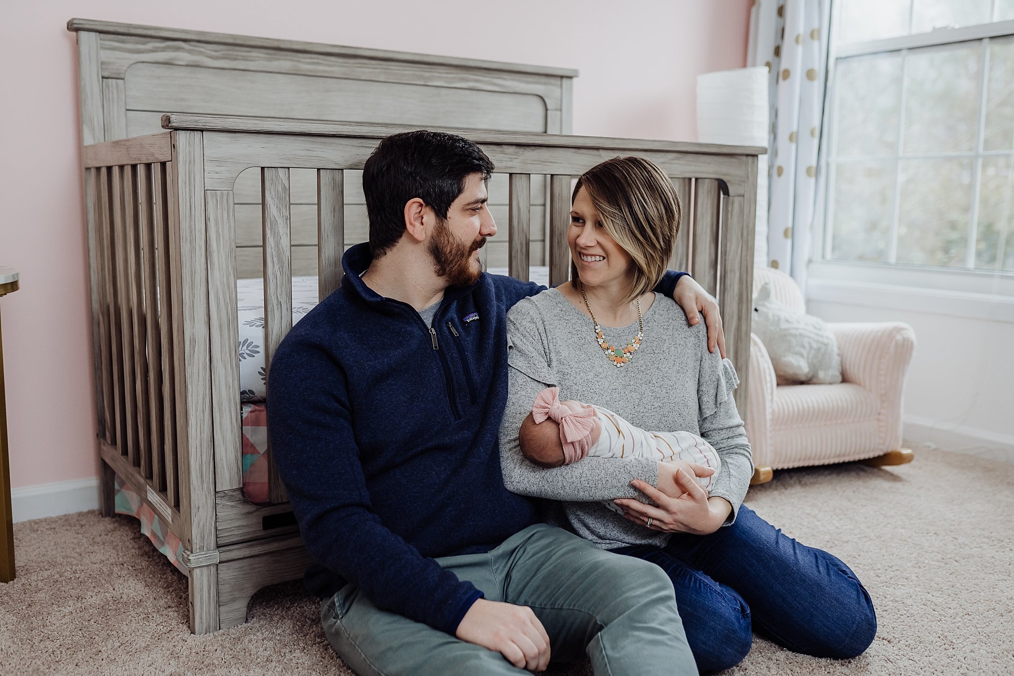 family of 3 sitting in front of crib at lifestyle newborn session