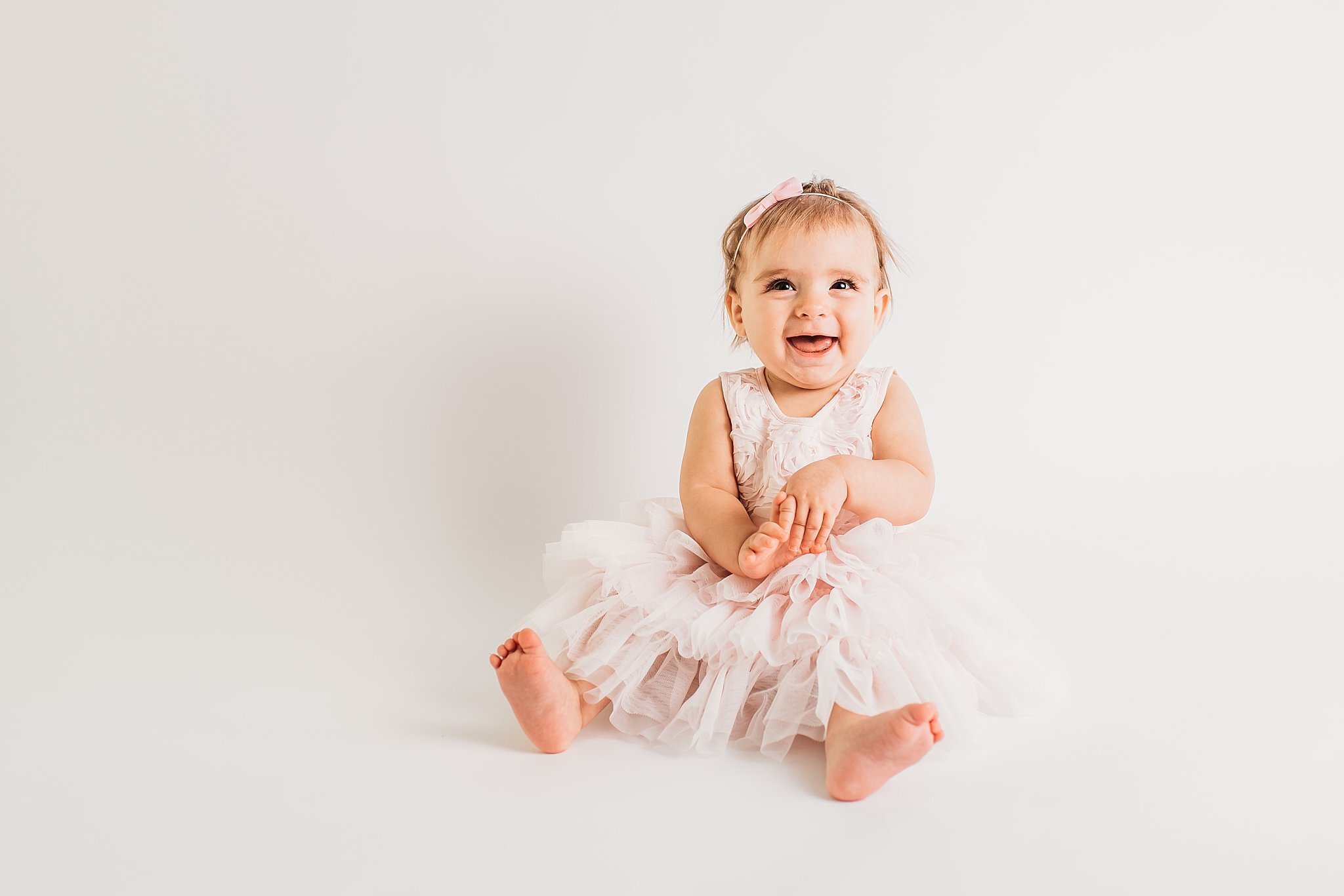 Baby girl sitting on white backdrop in pink dress  | Atlanta Baby Photographer