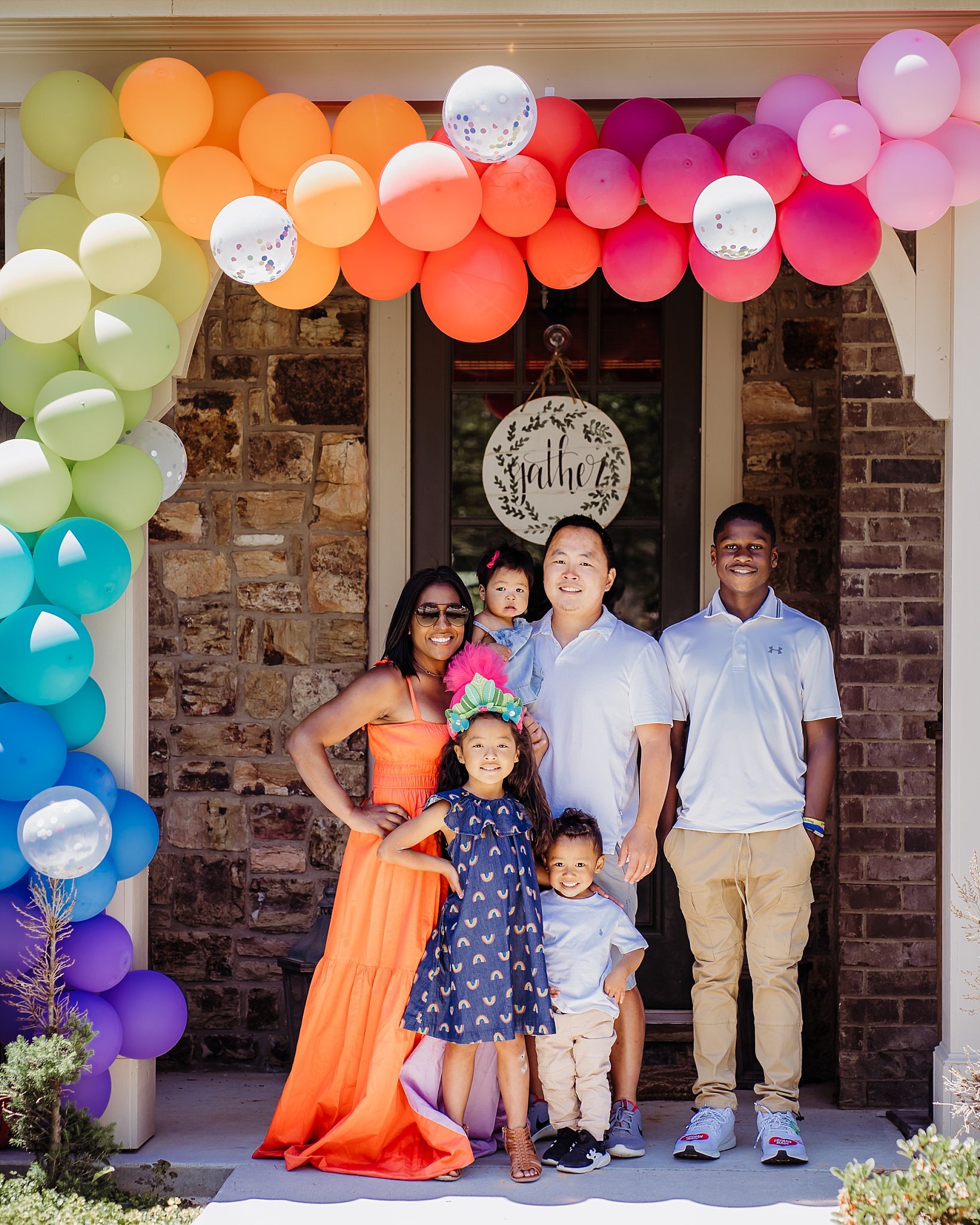 family on front porch under rainbow balloon arch 