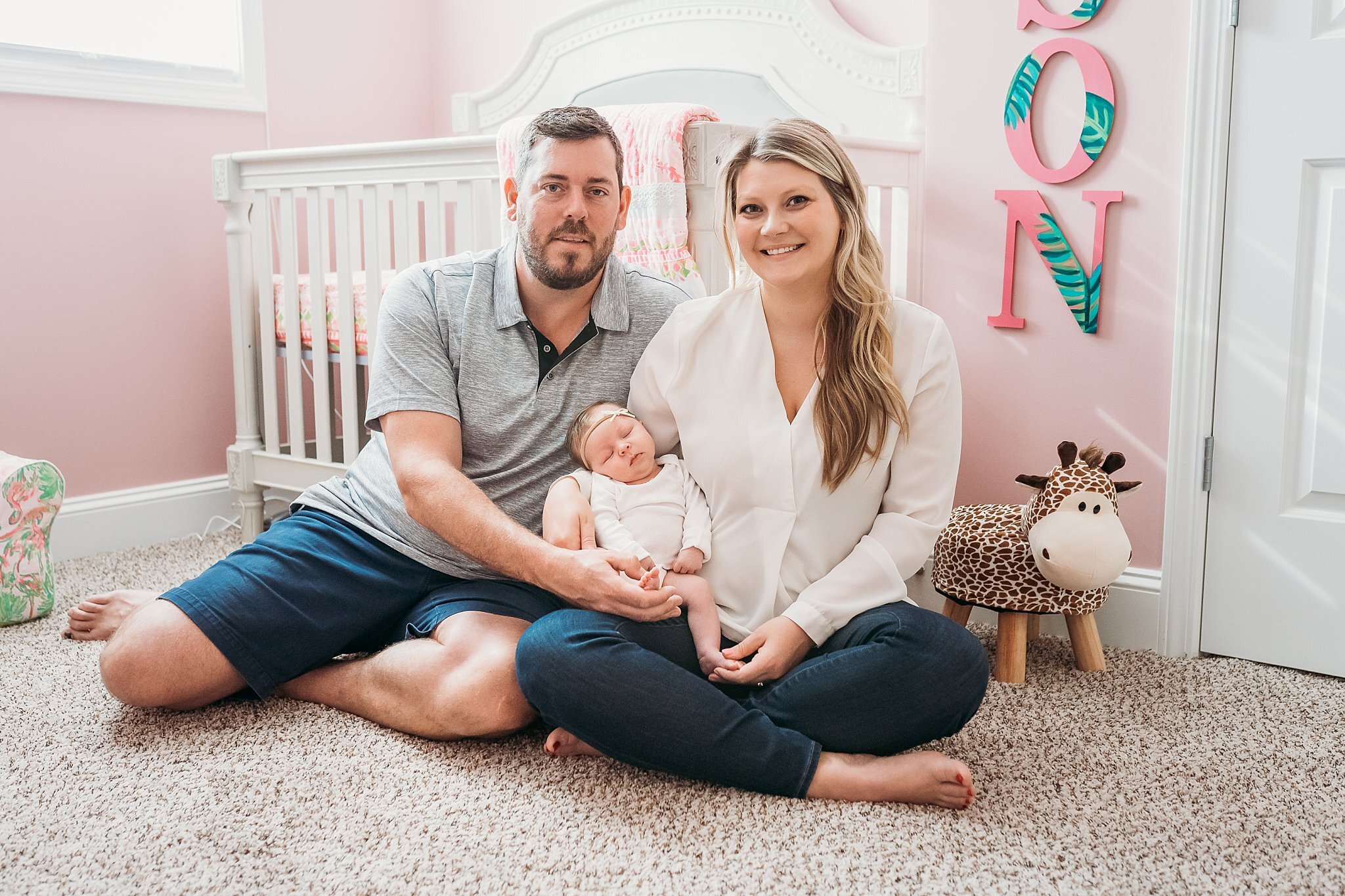 Family with newborn baby girl sitting in front of crib in pink nursery | Atlanta In Home Newborn Session