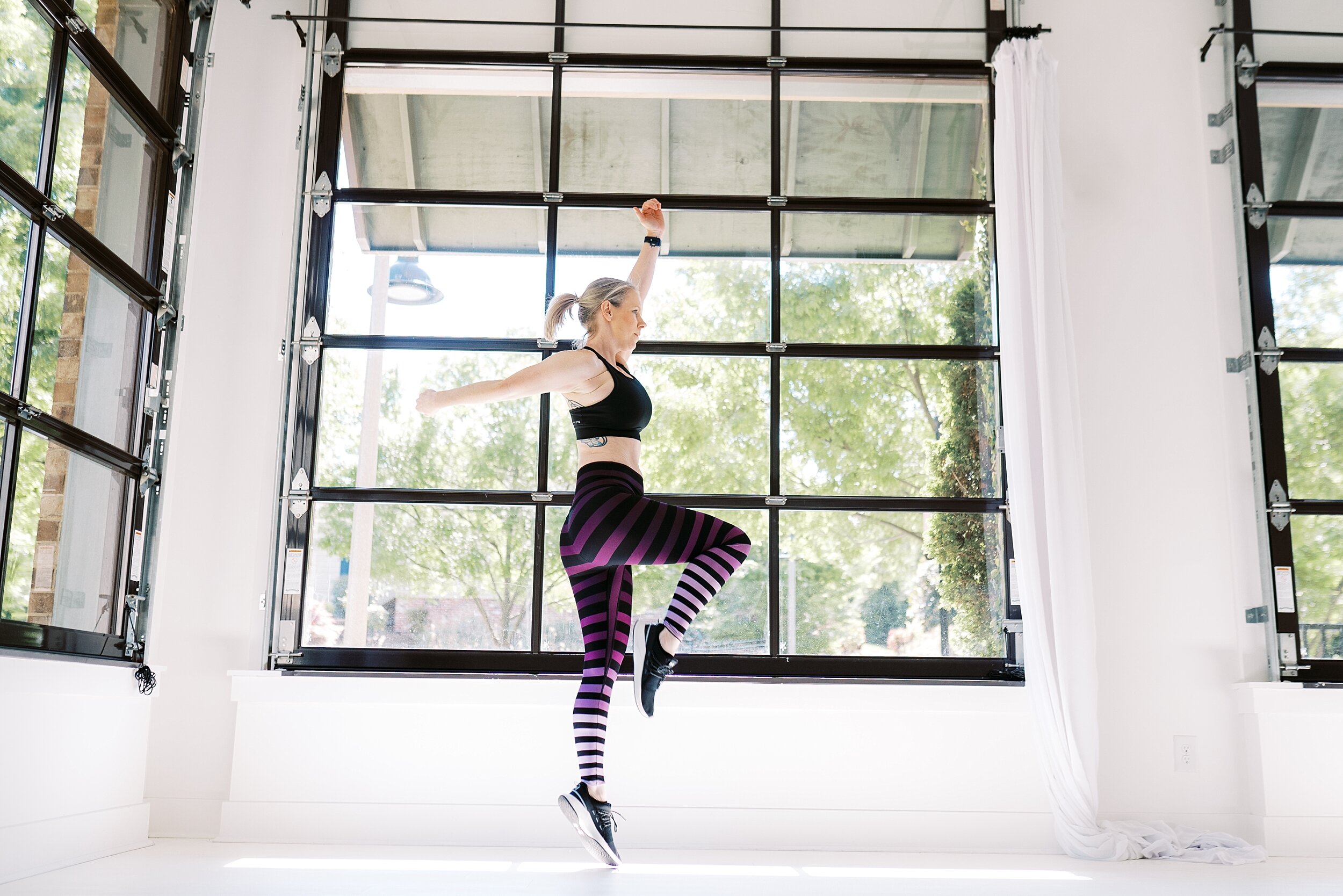 Atlanta Fitness Blogger jumping in front of windows at Whitewall Woodstock