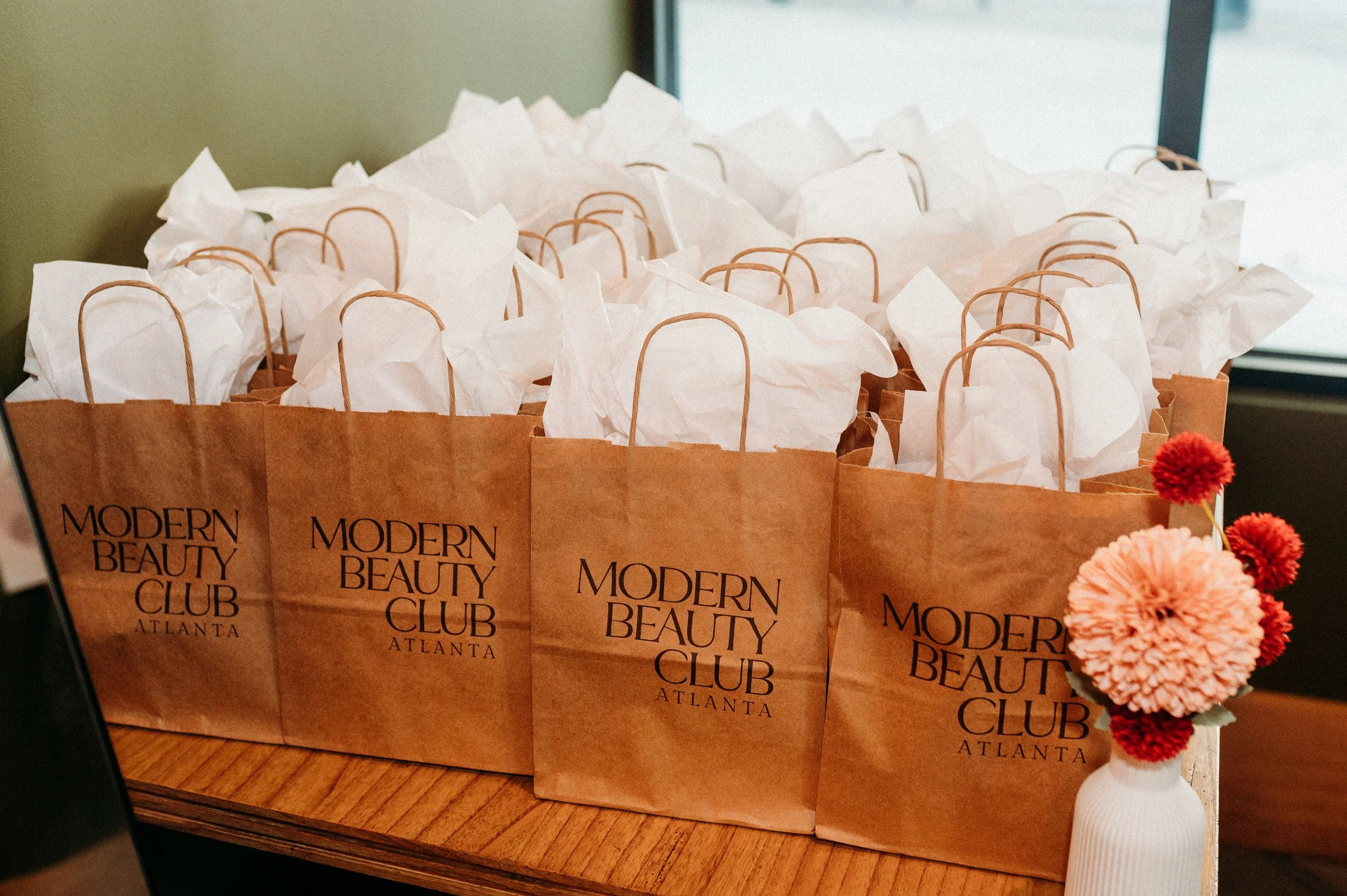 Rows of brown paper bags with "Modern Beauty Club" printed on them, filled with white tissue paper.