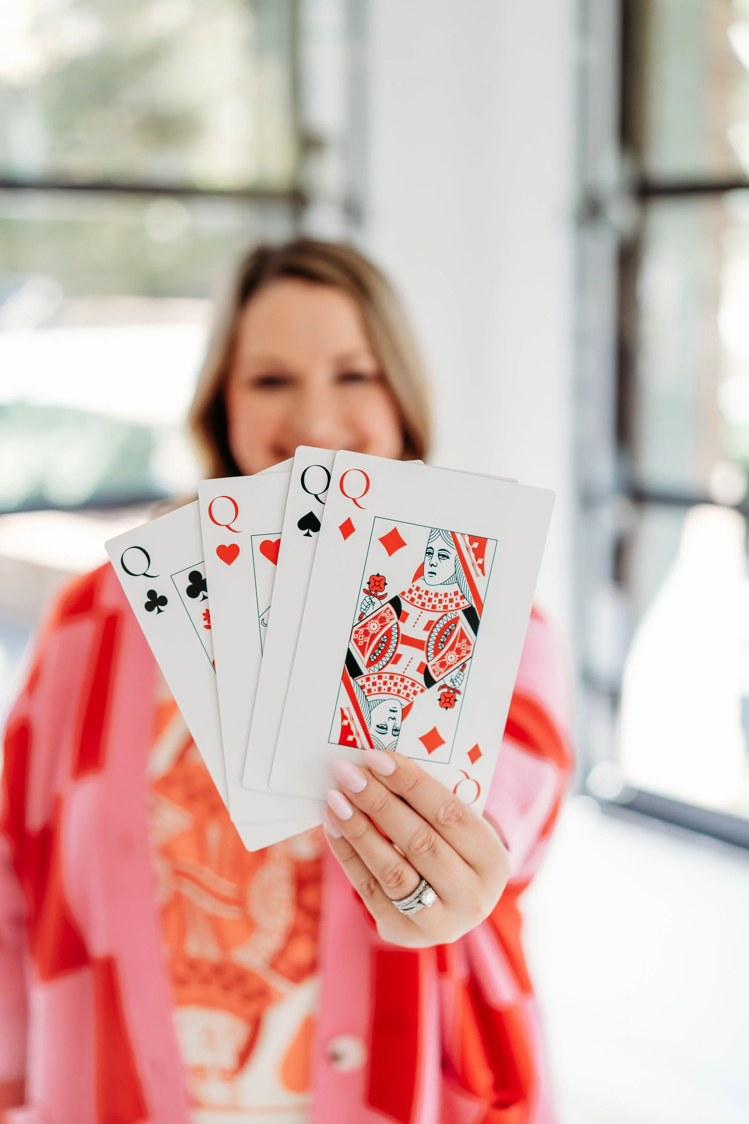 woman holding out oversized queen cards from all in deck in front of windows at WHite Wall Studio in Woodstock, GA