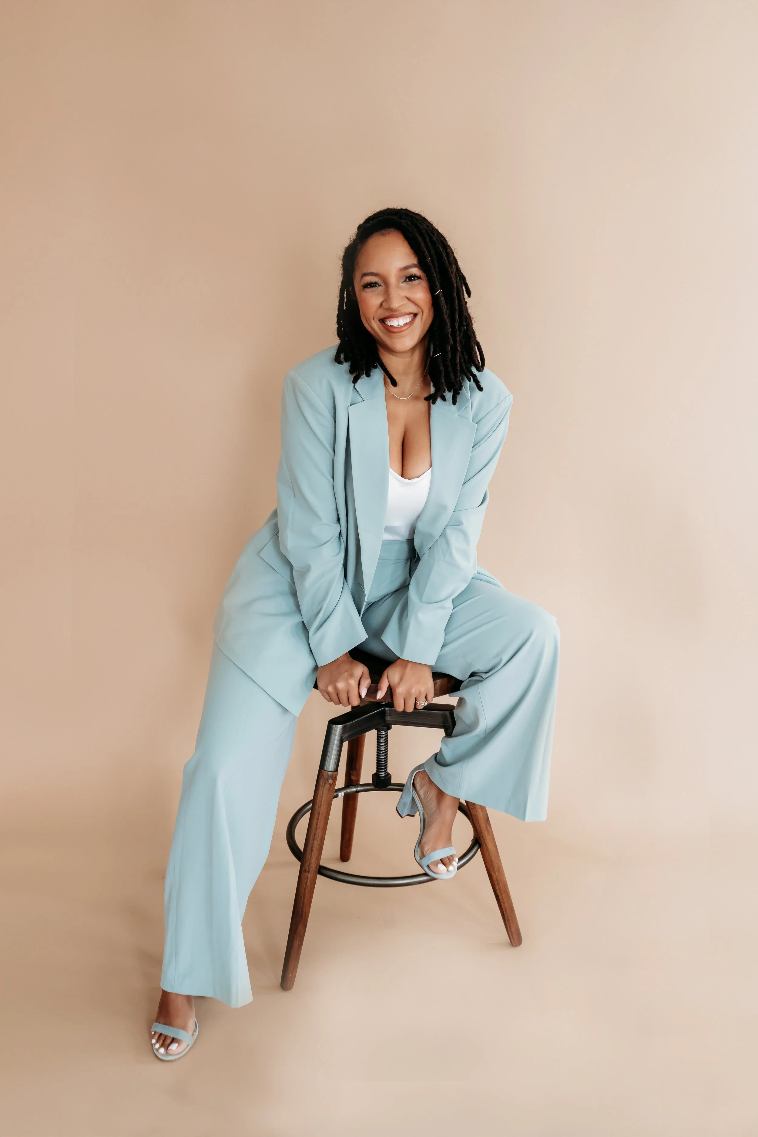 woman in blue suit posing for brand photos on stool against tan backdrop