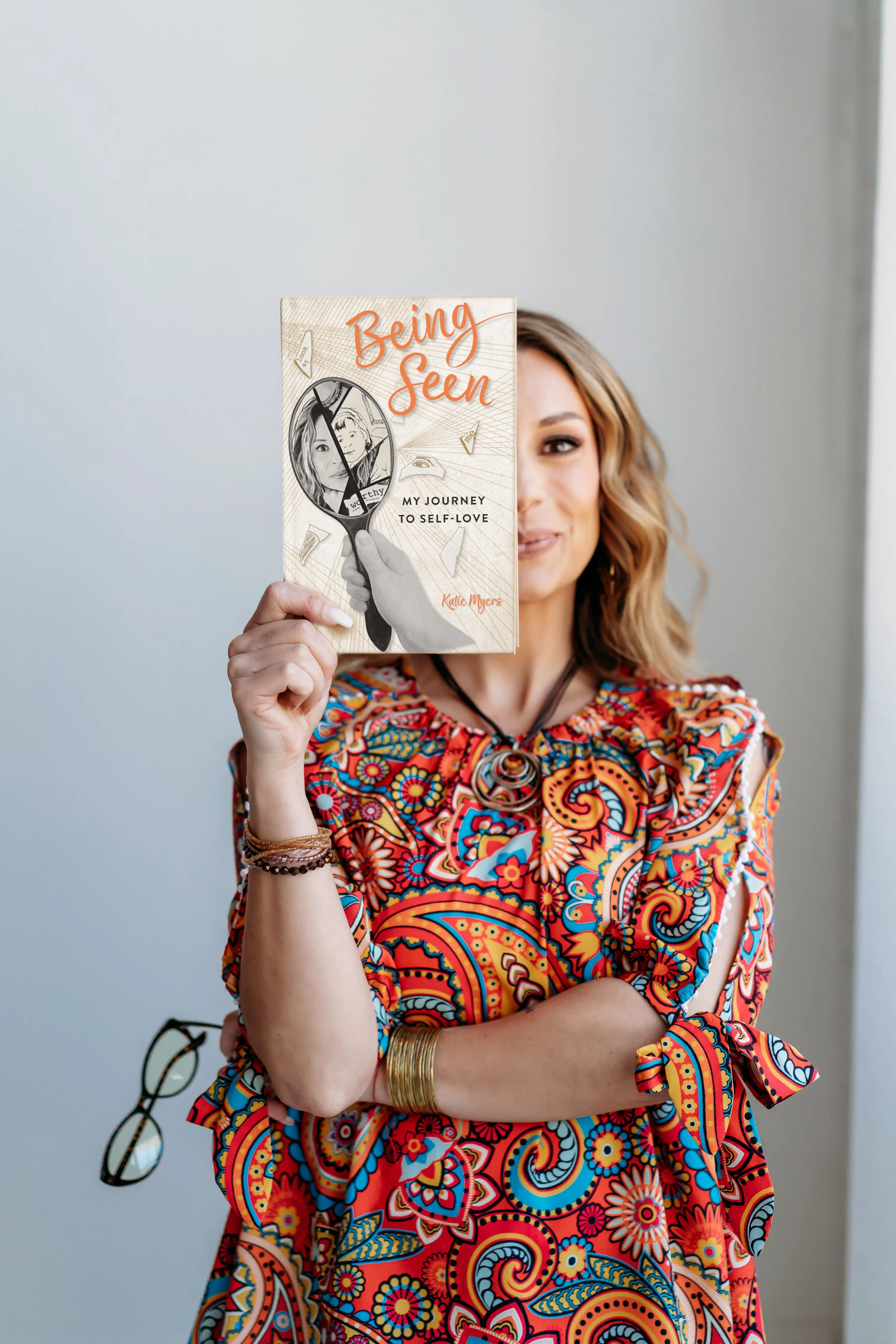 Lifestyle brand photo of Atlanta author holding book in front of face in bright paisley shirt
