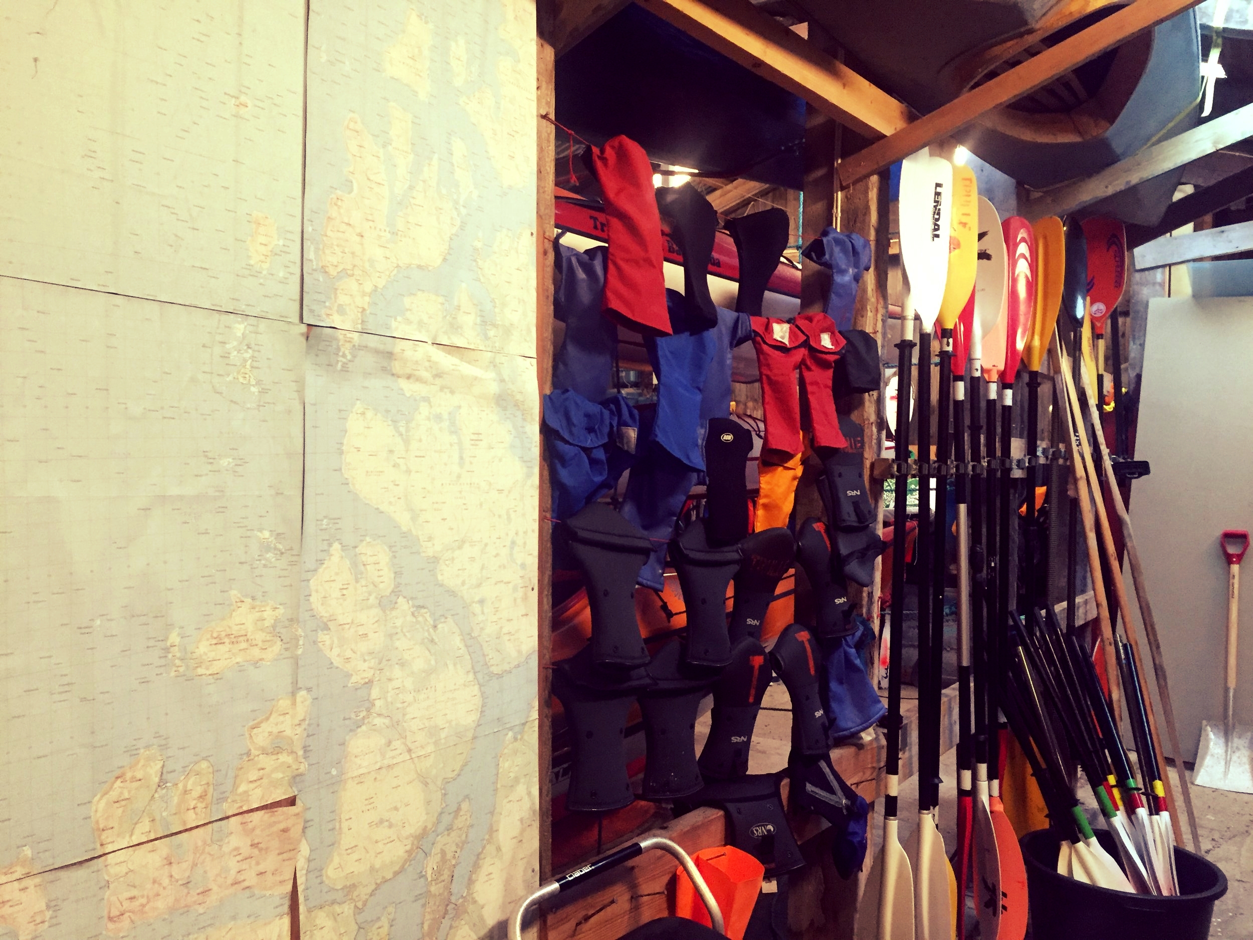 The inside of our boathouse with gear available for members, like pogies (mitts for your hands while padling) and padles, and a giant map of the area to plan your next paddling adventure.