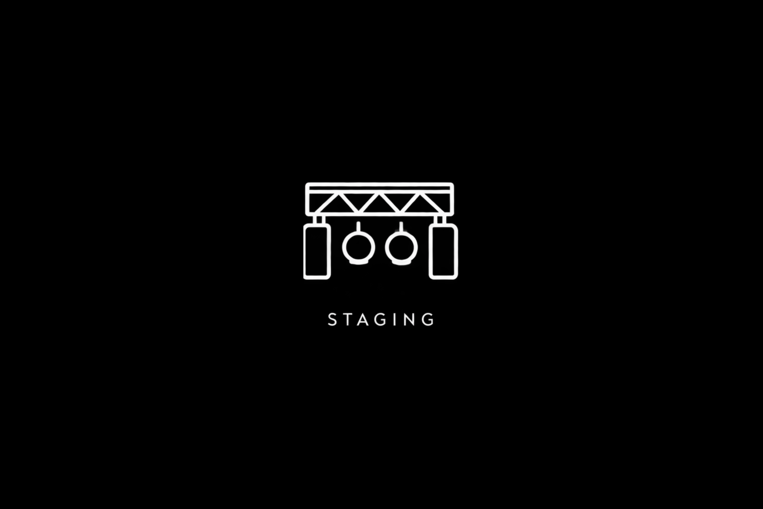 Simple line drawing of stage lighting equipment with the word 'STAGING' underneath, on a black background.