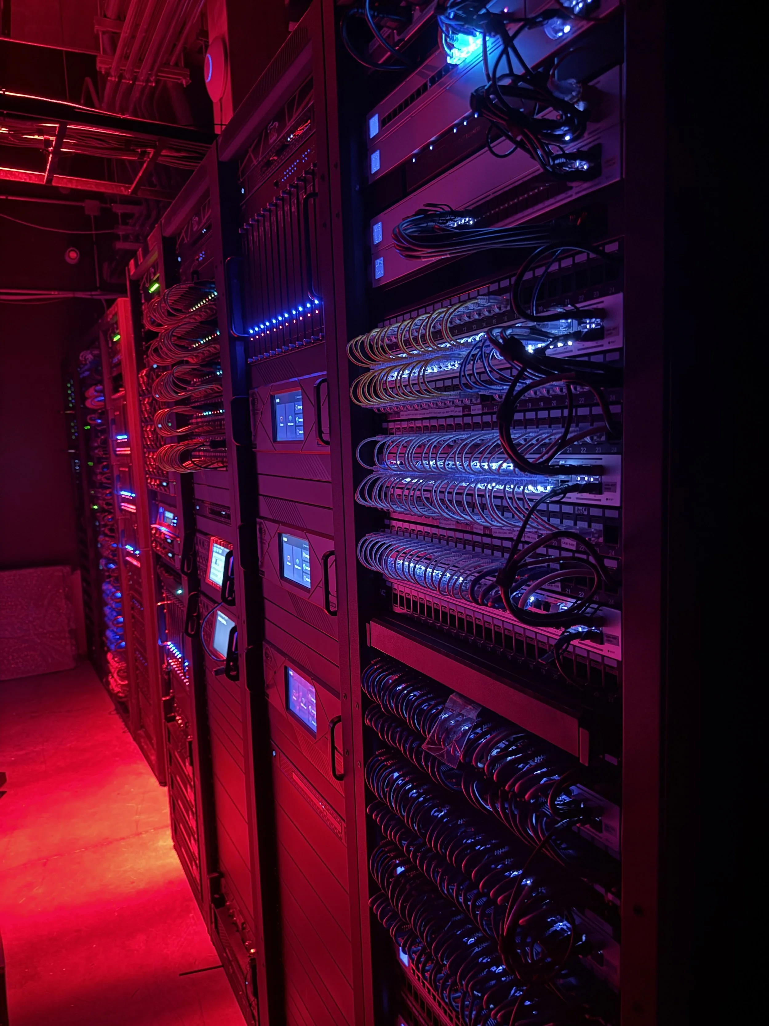 Rows of computer servers in a data center illuminated by pink and blue LED lights.
