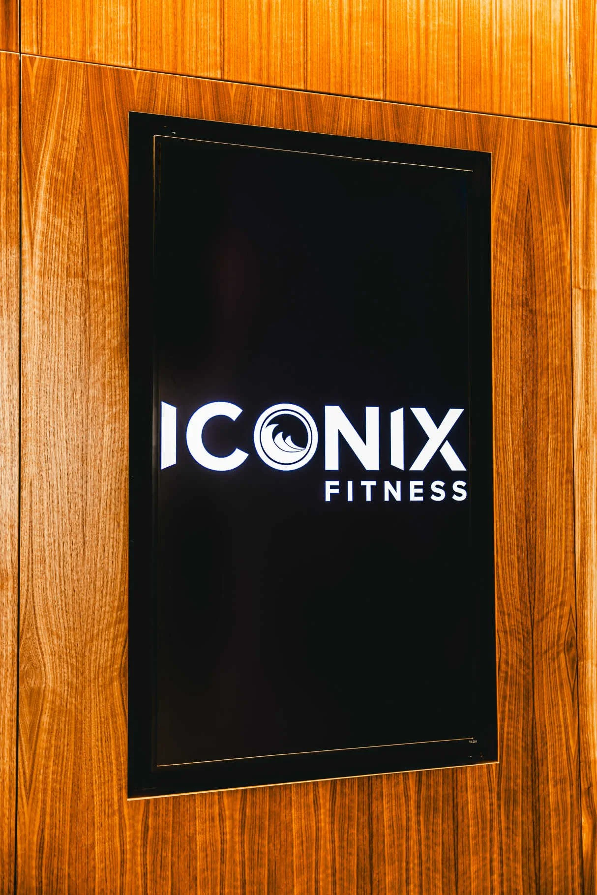 Sign for ICONIX Fitness mounted on a wood-paneled wall.