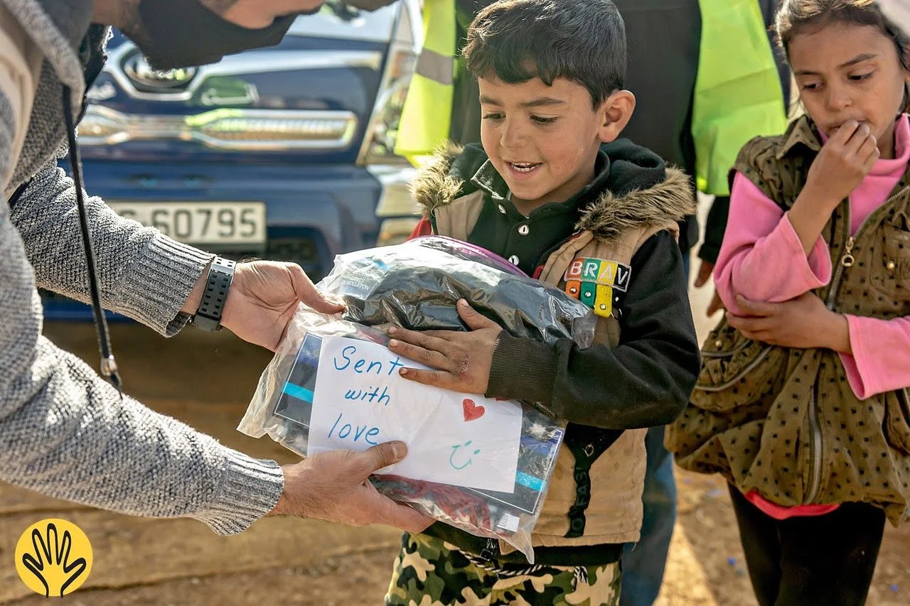    A Syrian refugee boy in Jordan receives some aid supplies, along with one of LHI’s signature 'You Are Loved' cards, which are included in every aid bundle.   