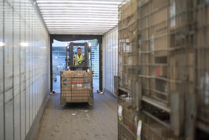 A forklift loads a truck containing parcels. This was shot with only available light.