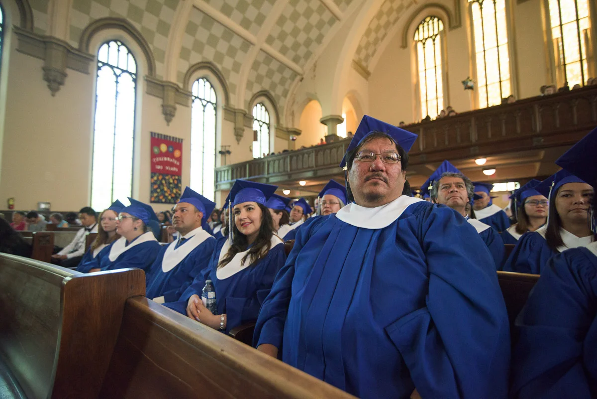 Rows of graduands seated on long benches listen to the commencement speeches. In this wide shot, the background is kept in focus in order to capture the grandeur of the ceremony hall.