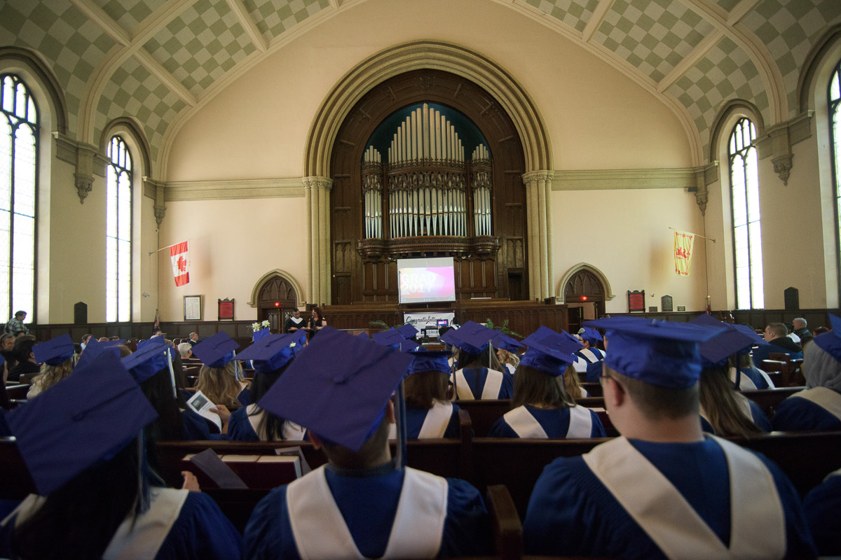 This photograph captures the rows of seated students and the area above them reaching up to the high vaulted ceiling. This perspective emphasizes the architectural features of the space, and provides a sense of its size and the number of people in the room.
