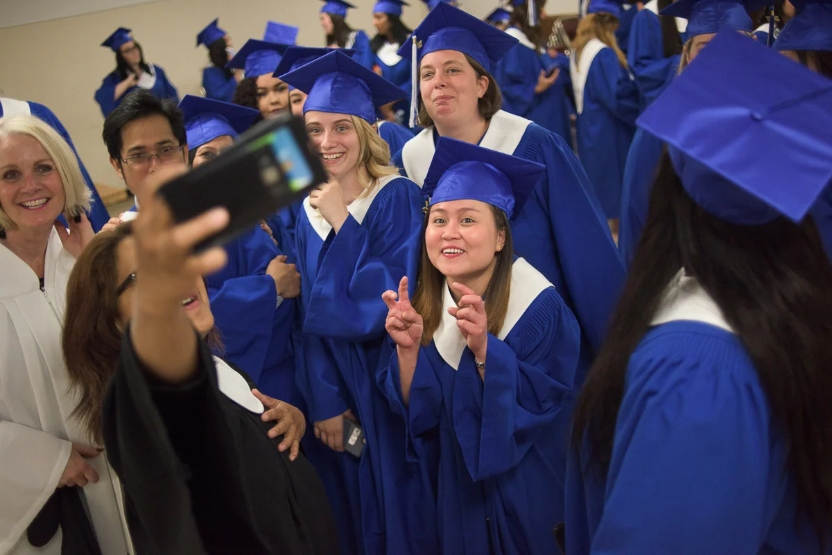 There is a lot of activity in this photograph, which features a group of students and instructors taking a group shot using a phone. The photograph conveys the celebratory atmosphere of the event.