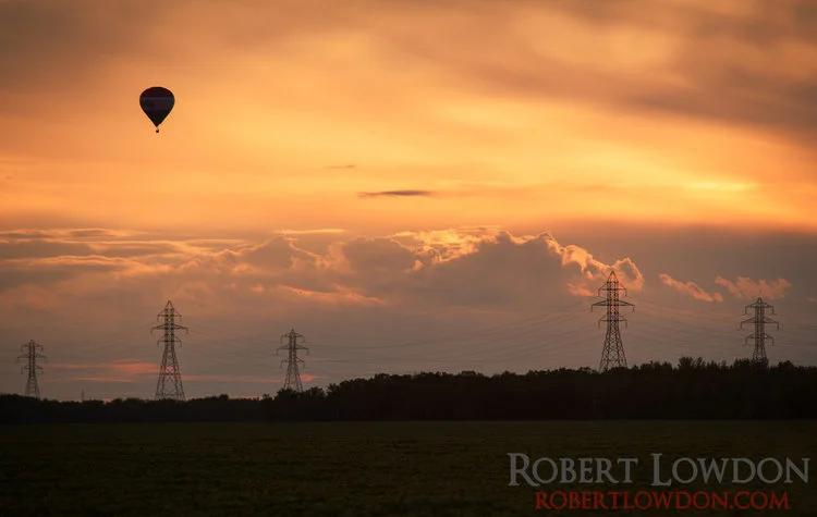 The Great Winnipeg Balloon Attack. The sun sets over the prairies with a hot air ballon in the background