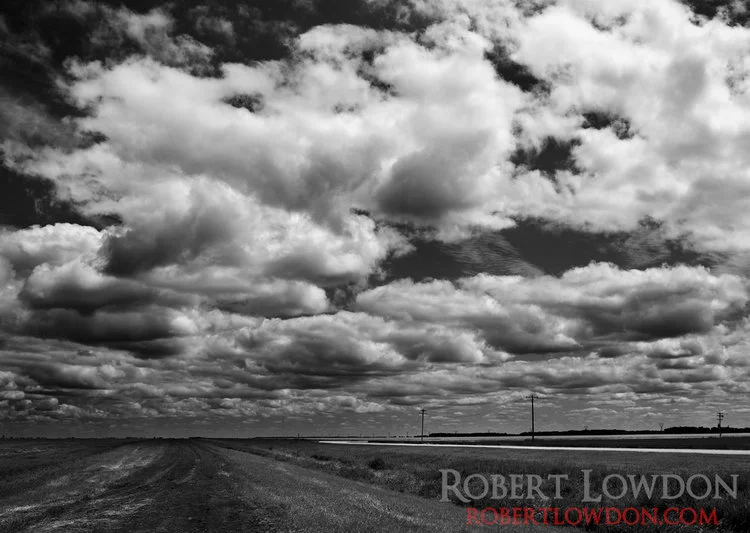 Clouds move across this prairie landscape. © Robert Lowdon The prairies are best known, for well, how flat they are. The epic skies and fields of endless clouds, seem to be less well known. Here we have a black and white photograph taken in mid day. Can you count how many clouds are in this photo?