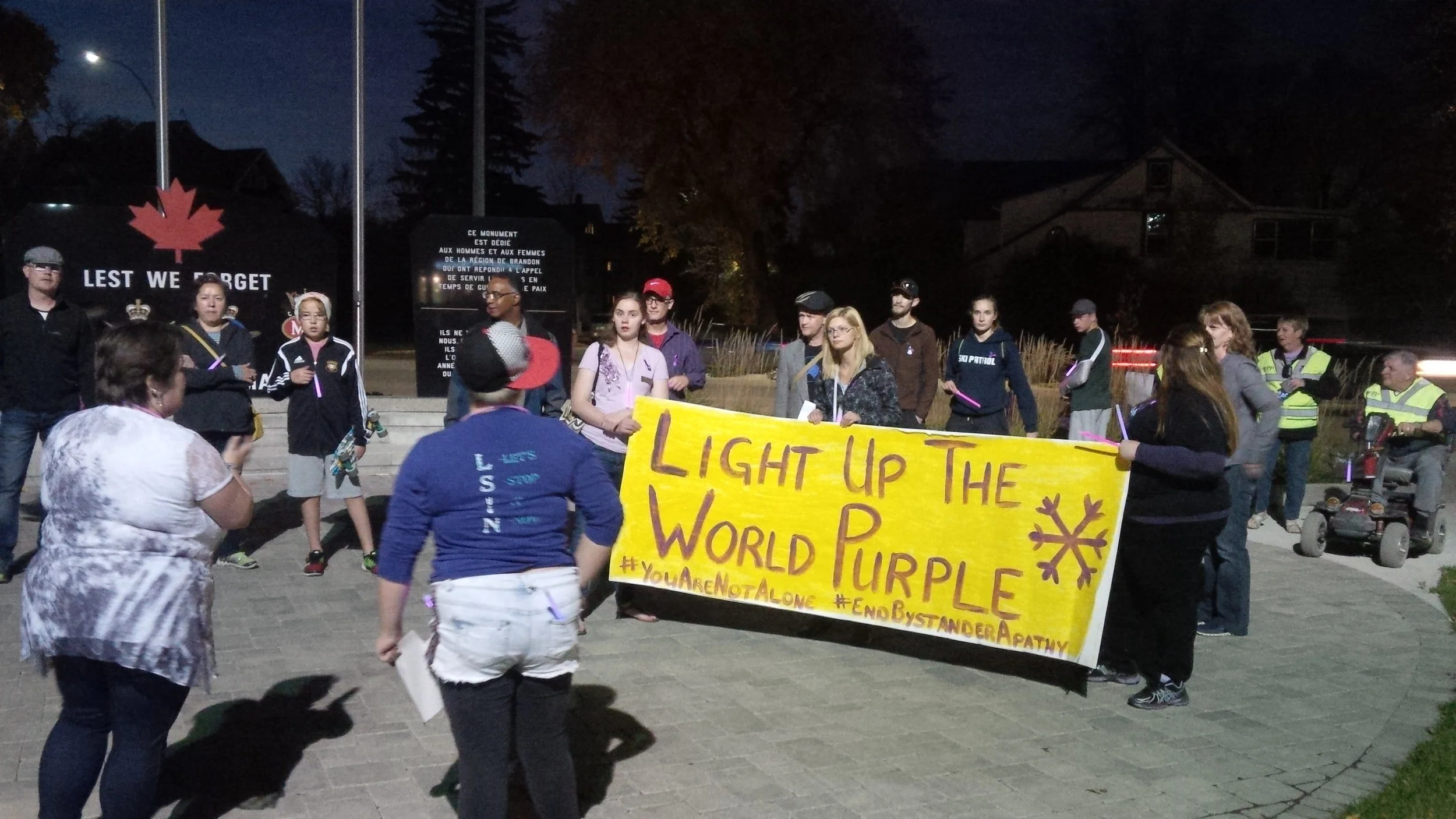 Participants hold a banner at the war memorial outside the Brandon Police Service at 2015's Light Up the World Purple walk. (Logan Praznik/The Quill)