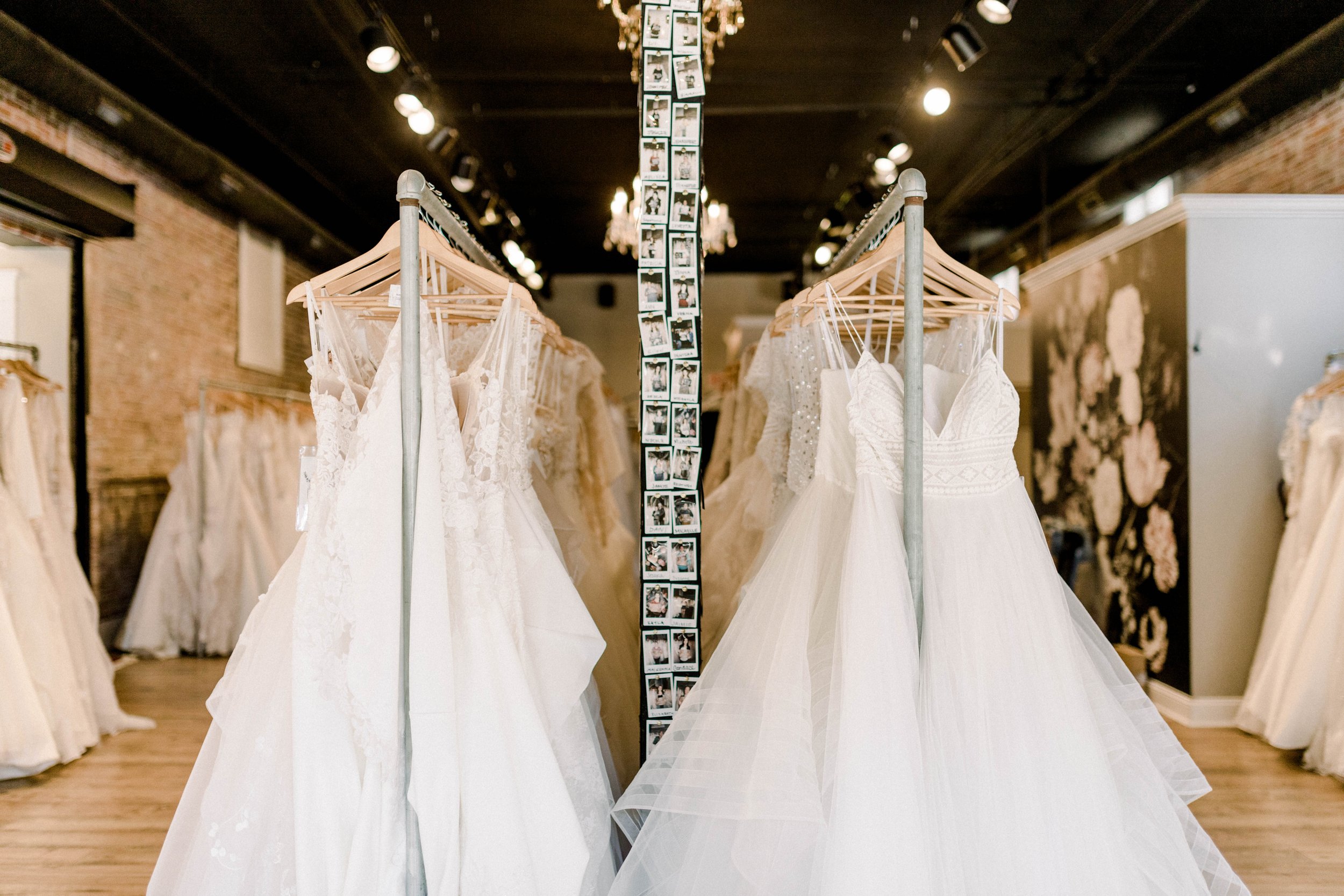 Bridal gowns hanging on wooden hangers in a bridal shop with brick walls and black ceilings